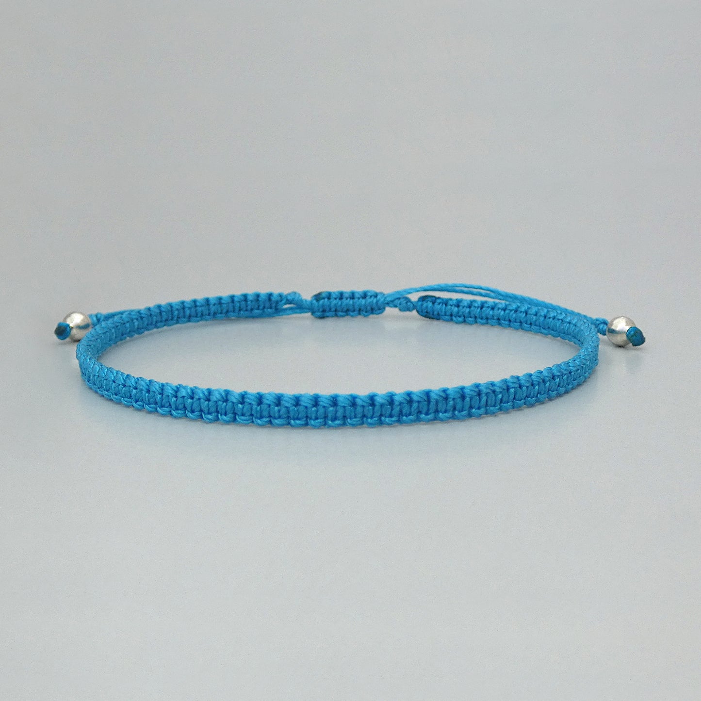 7” adjustable Bermuda blue macramé bracelet for adults with silver plated bead ends.