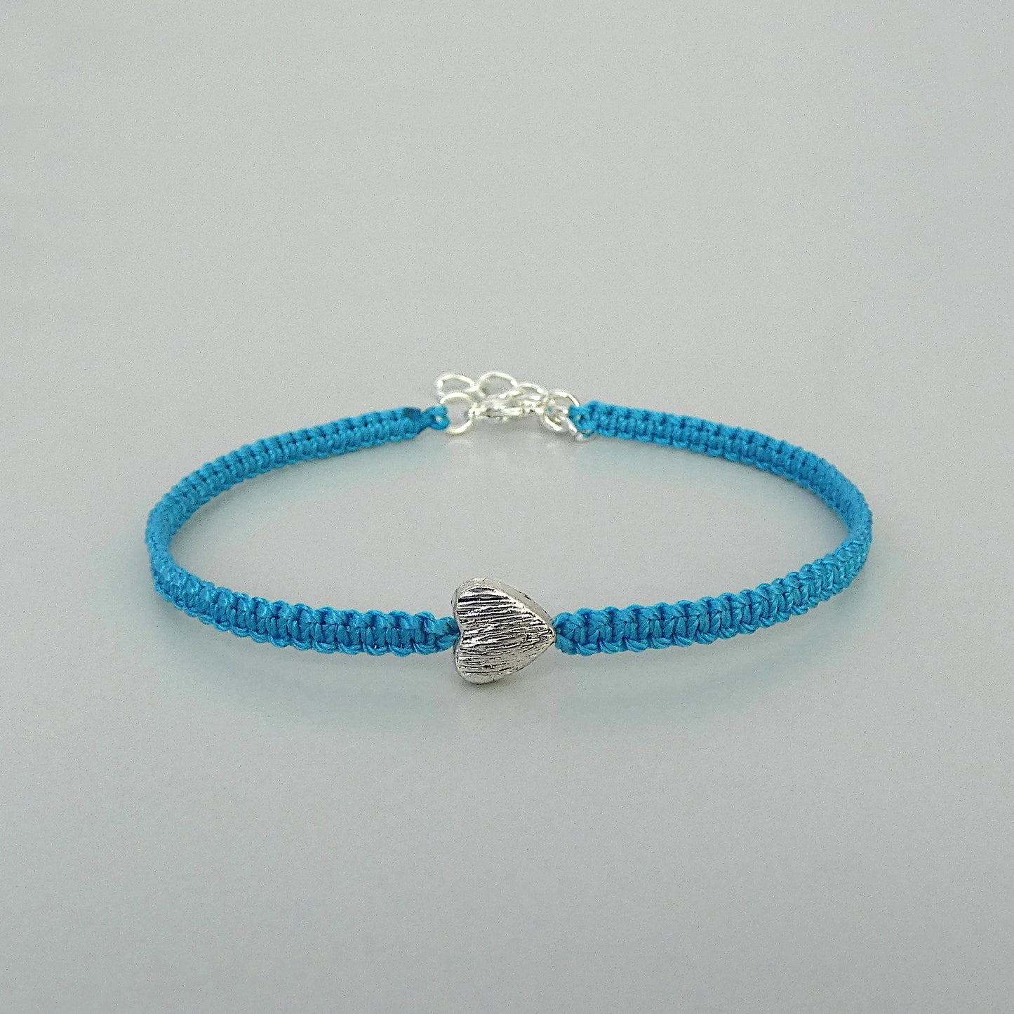 Blue seven inch macramé bracelet with silver plated textured heart charm, lobster clasp and one inch extender chain.