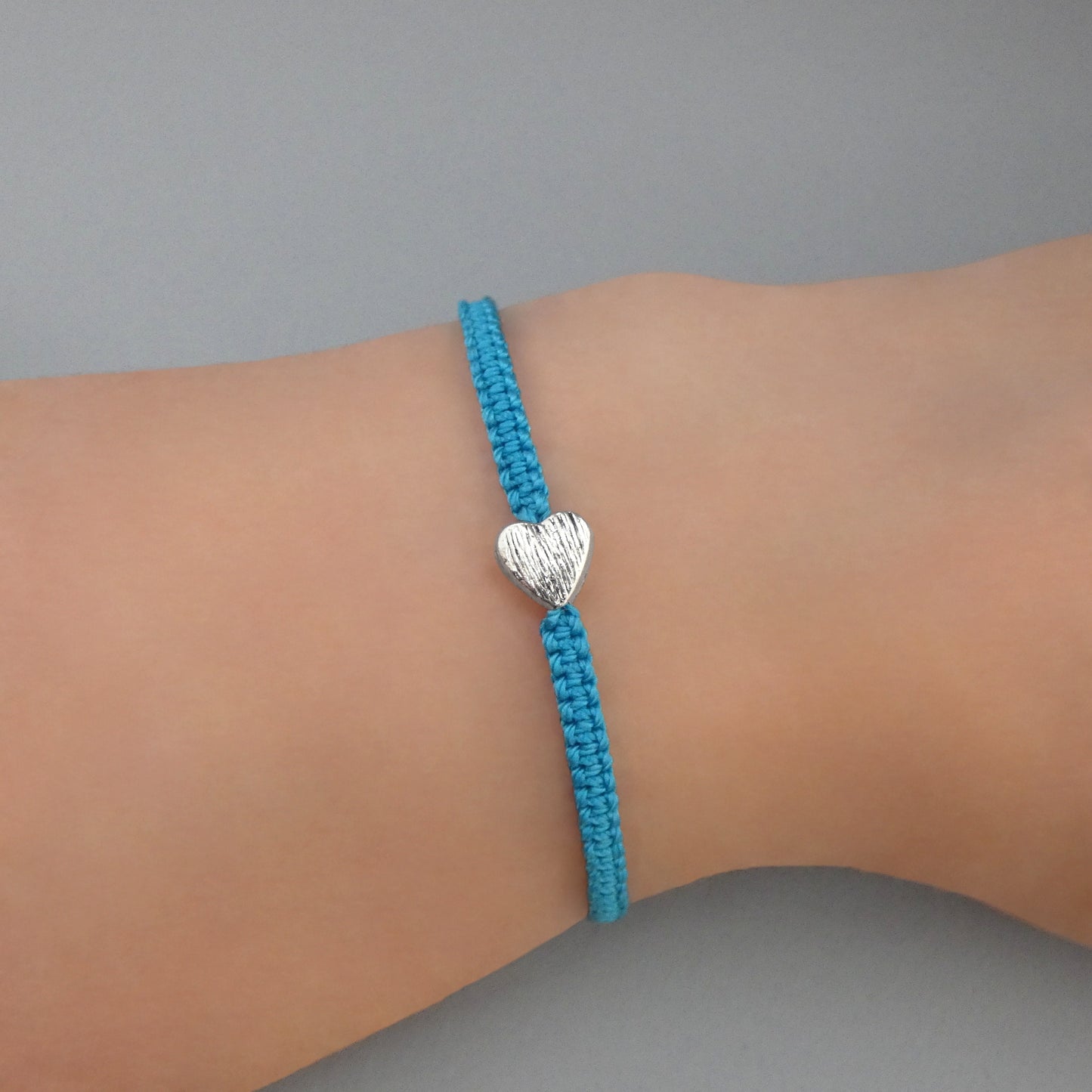 Blue seven inch macramé bracelet with silver plated textured heart charm, lobster clasp and one inch extender chain on a woman's wrist.