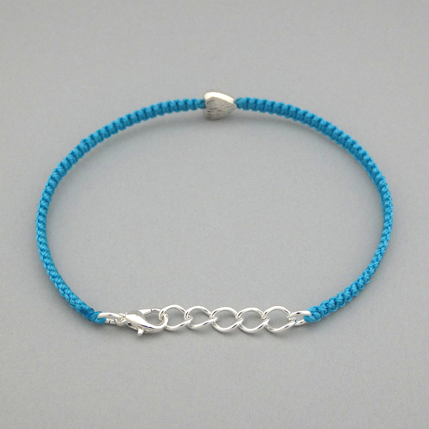 Blue seven inch macramé bracelet with silver plated textured heart charm, lobster clasp and one inch extender chain. The bracelet is fully extended using the extender chain.