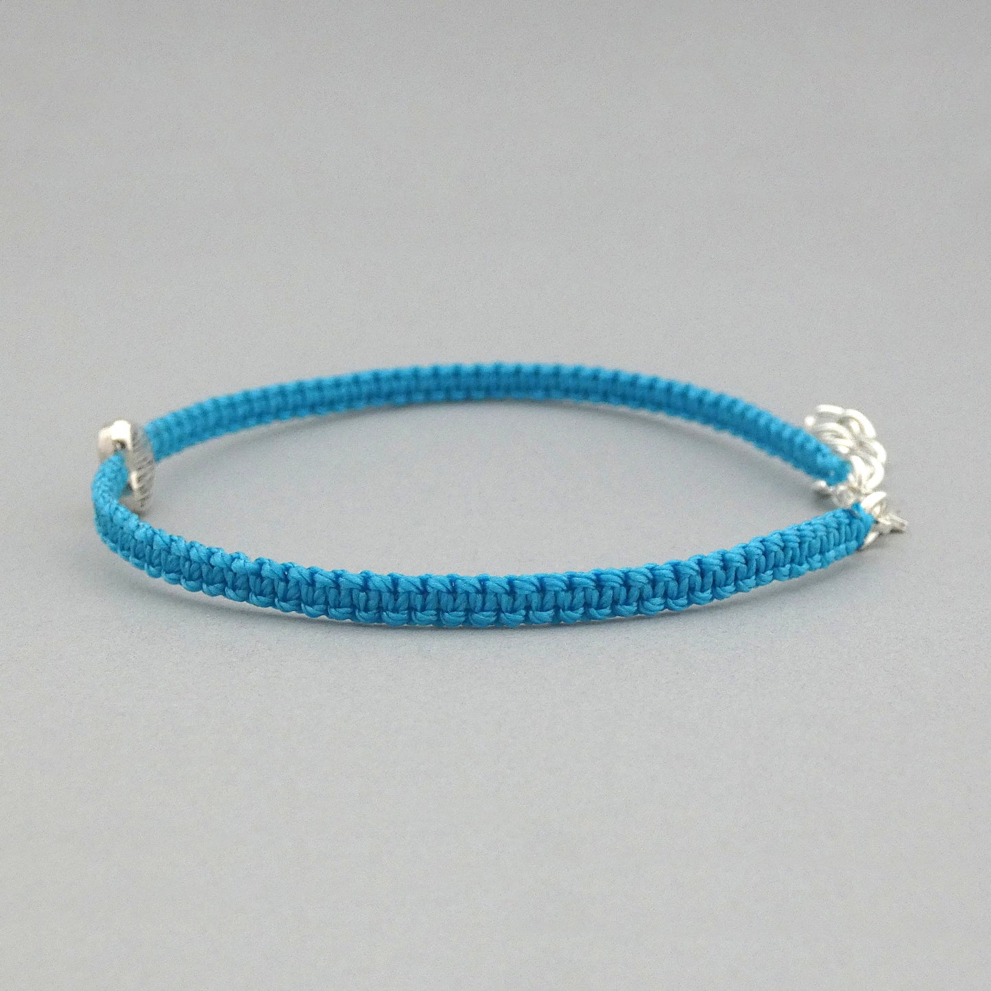 Side view of the knots on a blue seven inch macramé bracelet with silver plated textured heart charm, lobster clasp and one inch extender chain.