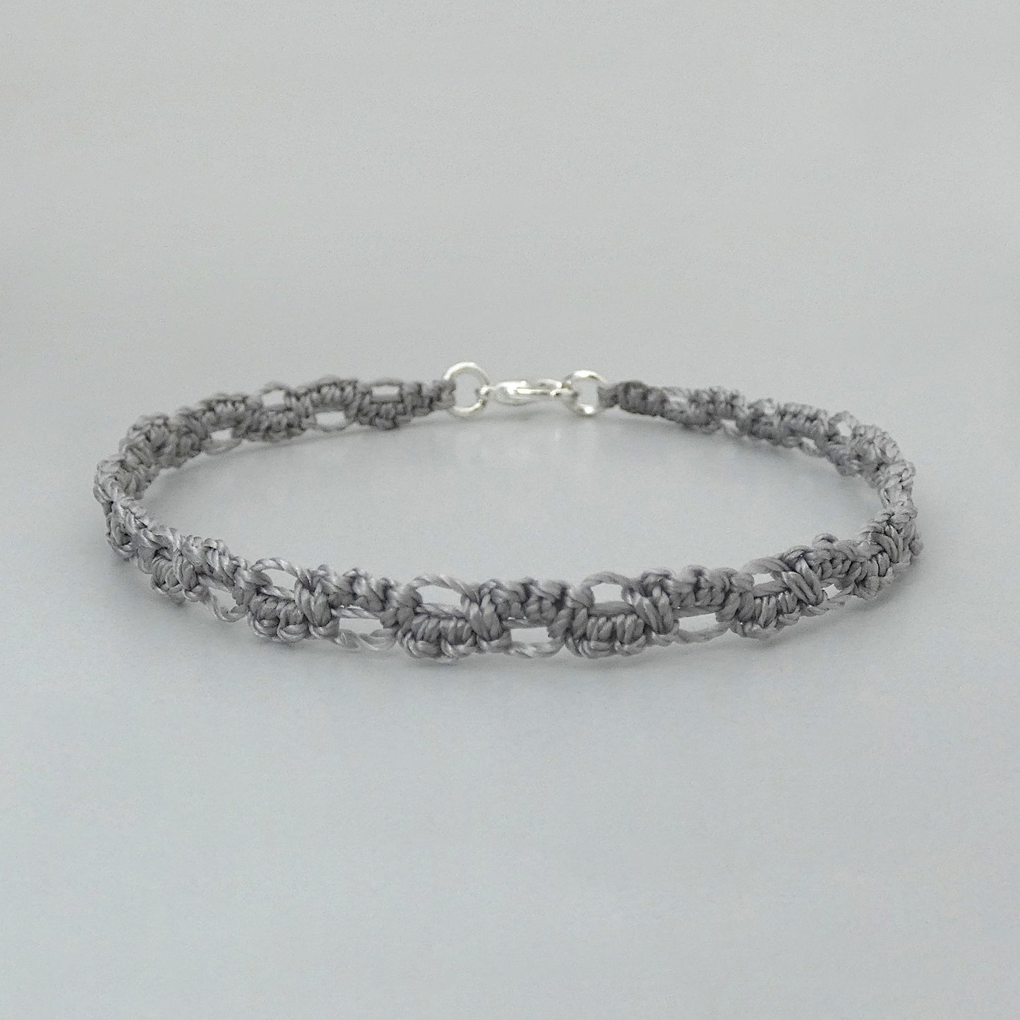 A silver grey macramé bracelet with a shiny silver plated clasp, displayed against a neutral background.