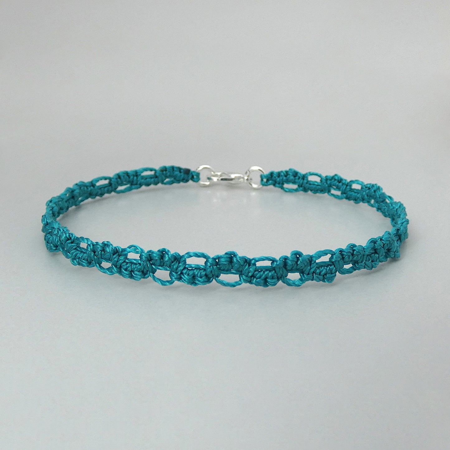 Teal green macramé bracelet tied with an intricate lace effect with silver plated clasp and optional 1” extender chain.