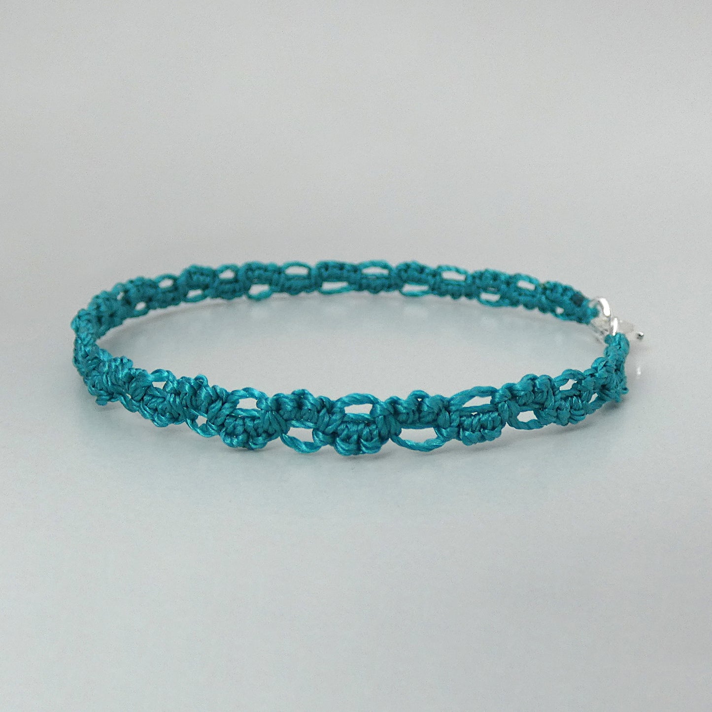 Teal green macramé bracelet tied with an intricate lace effect with silver plated clasp and optional 1” extender chain.