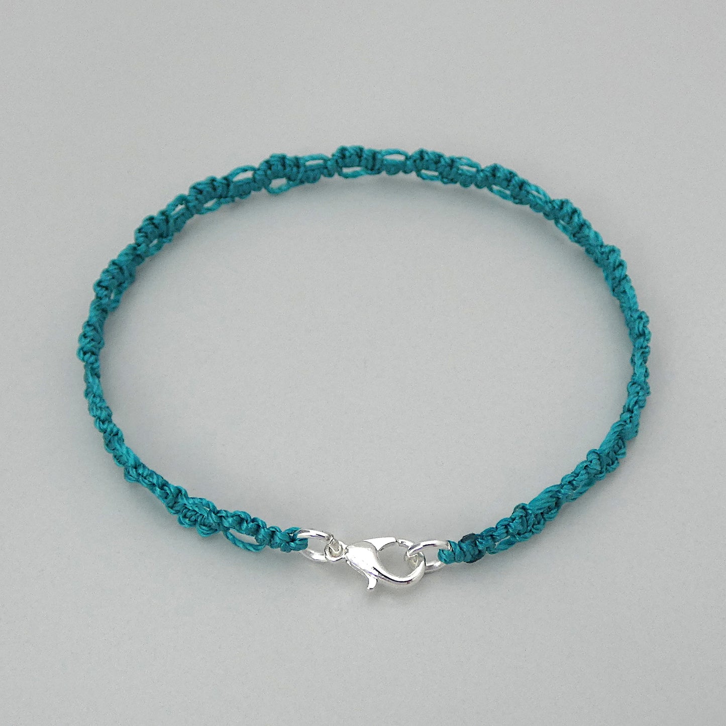 Teal green macramé bracelet tied with an intricate lace effect with silver plated clasp and optional 1” extender chain.