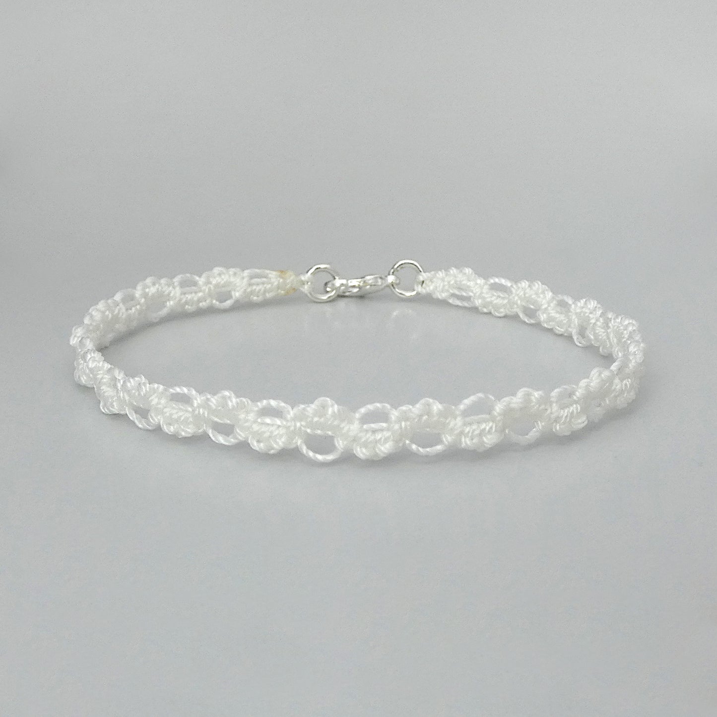 White macramé bracelet tied with an intricate wave effect with silver plated clasp and optional 1” extender chain.