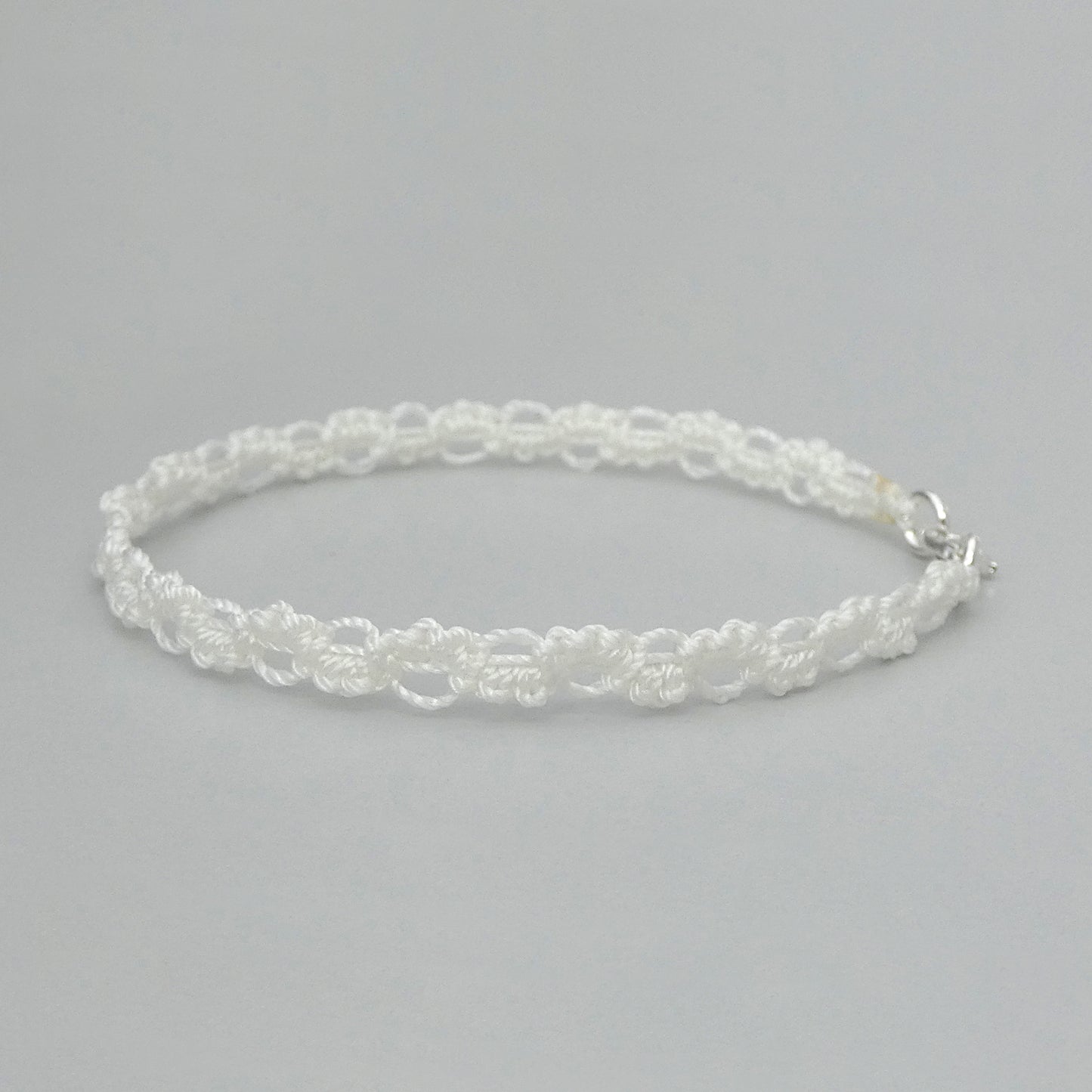 White macramé bracelet tied with an intricate wave effect with silver plated clasp and optional 1” extender chain.
