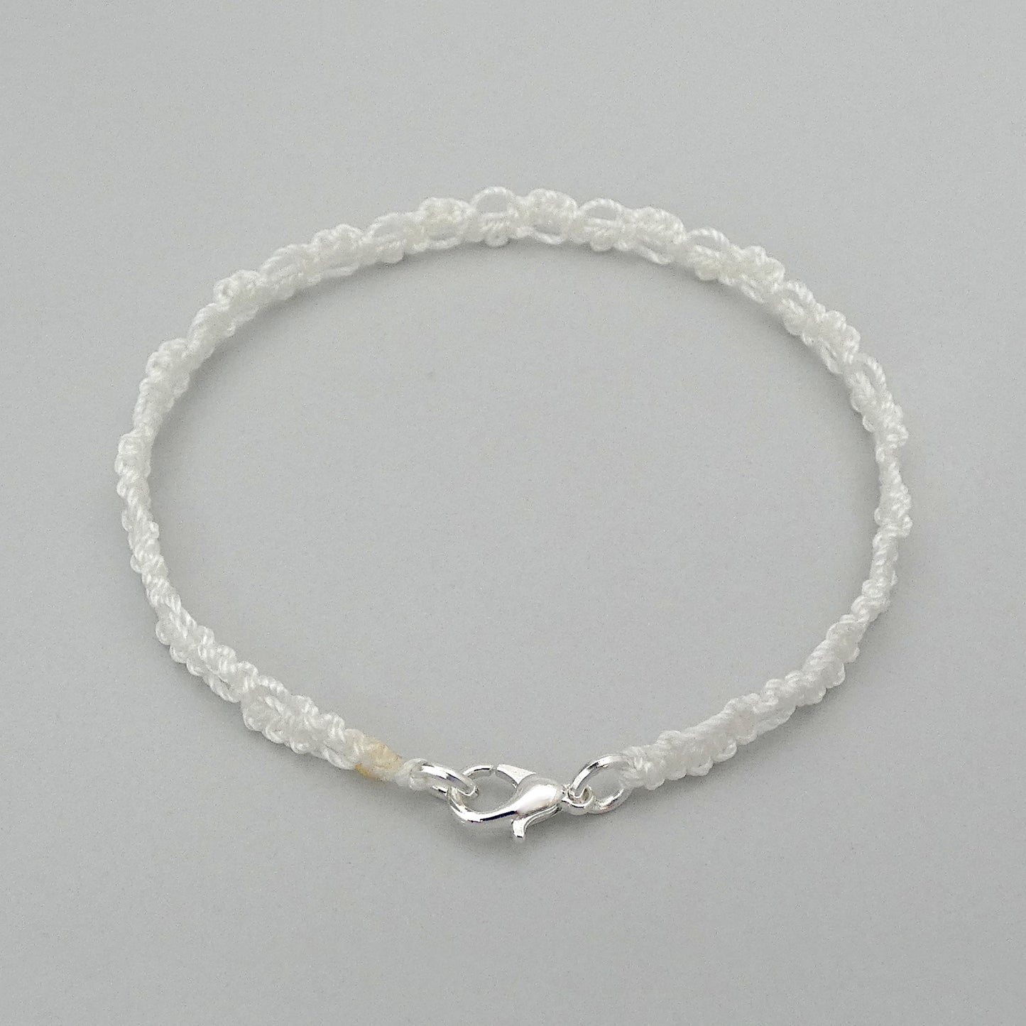 White macramé bracelet tied with an intricate wave effect with silver plated clasp and optional 1” extender chain.