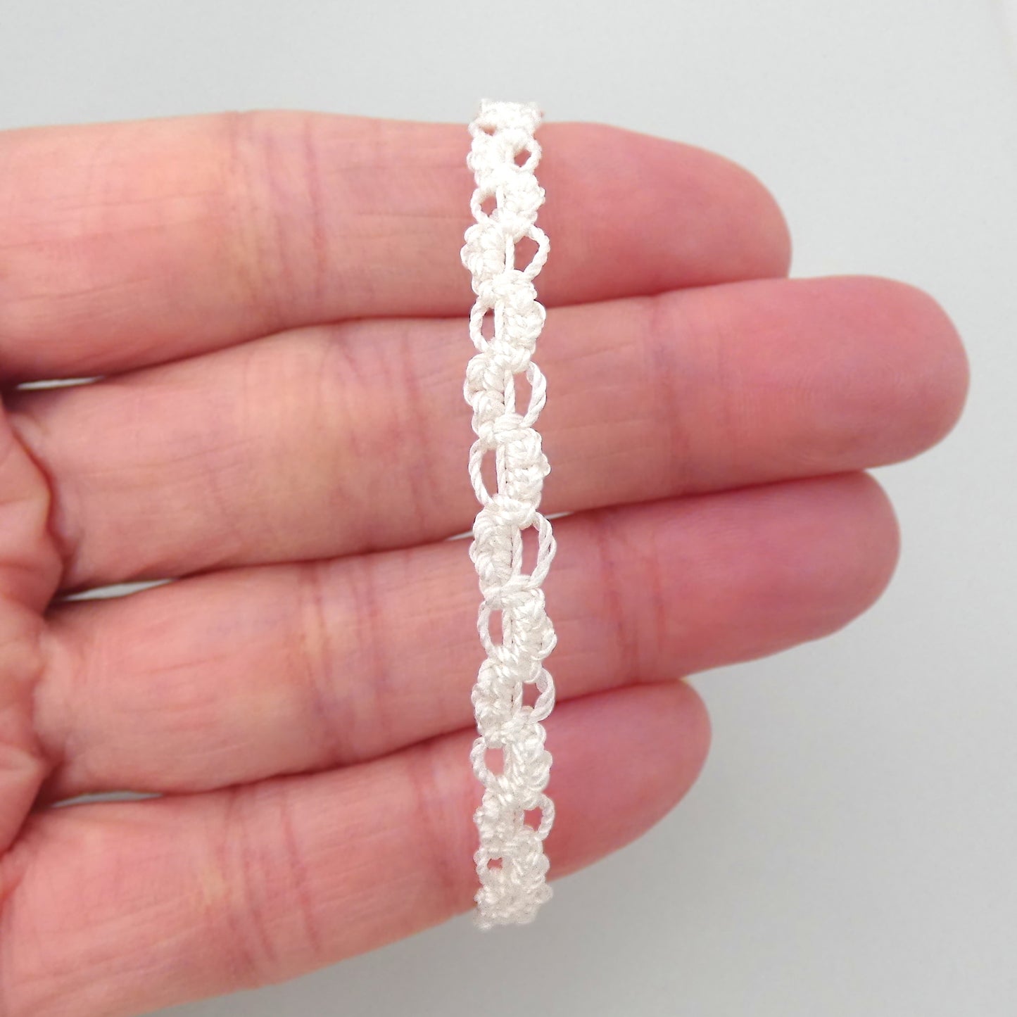 White macramé bracelet tied with an intricate wave effect with silver plated clasp and optional 1” extender chain.