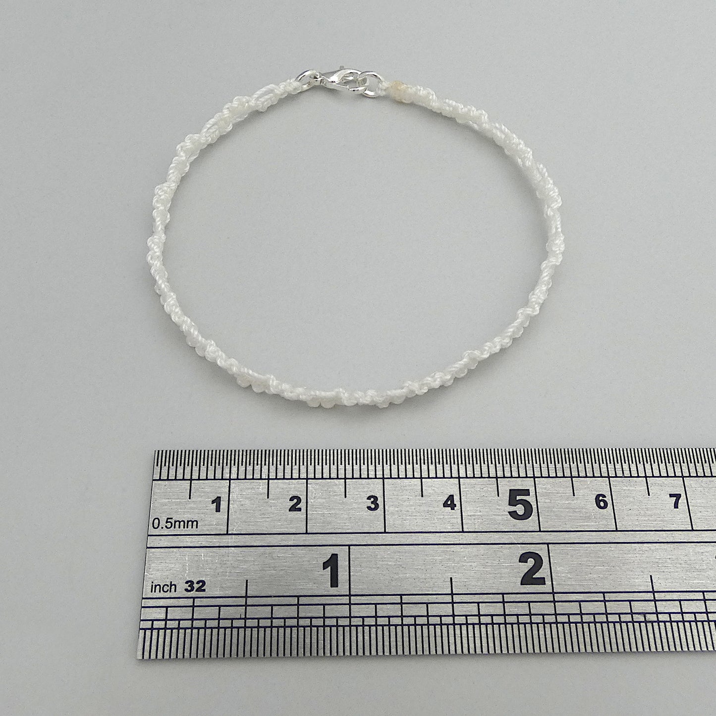 White macramé bracelet tied with an intricate wave effect with silver plated clasp and optional 1” extender chain.