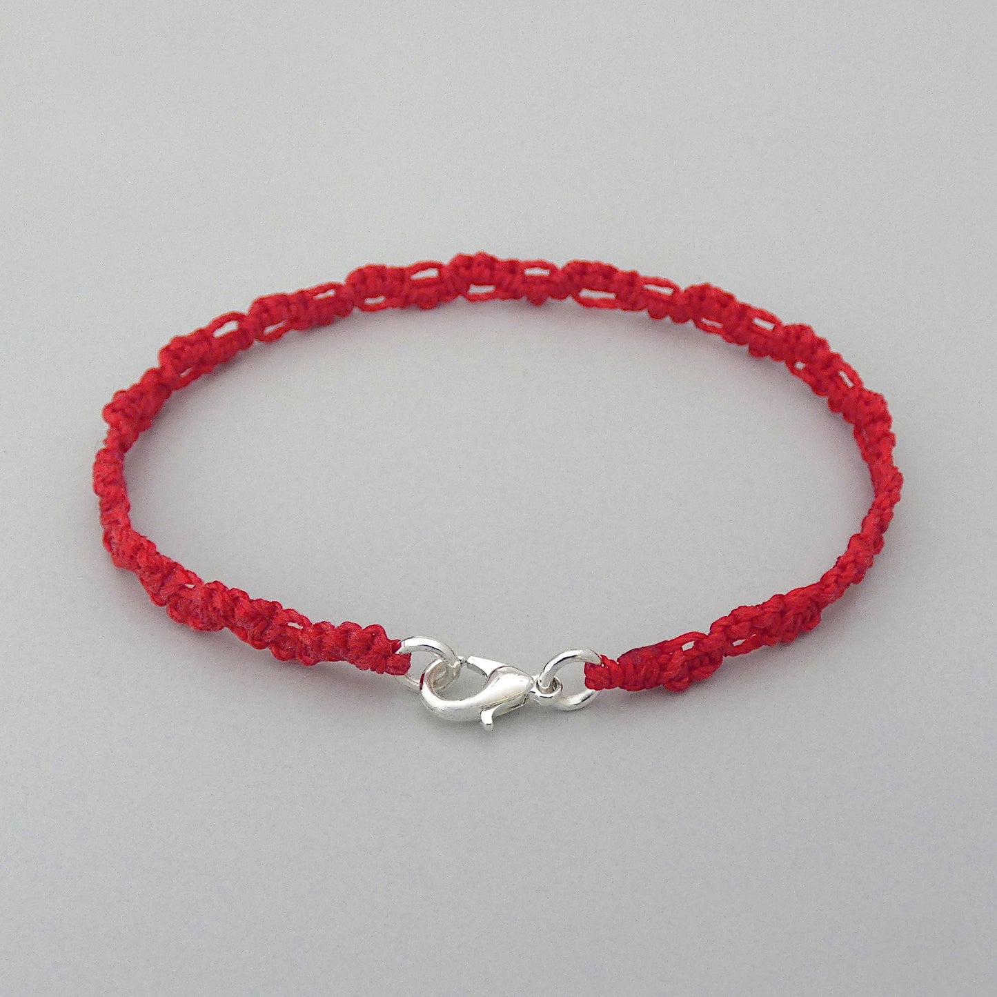 Red macramé bracelet tied with an intricate lace effect with silver plated clasp and optional 1” extender chain.