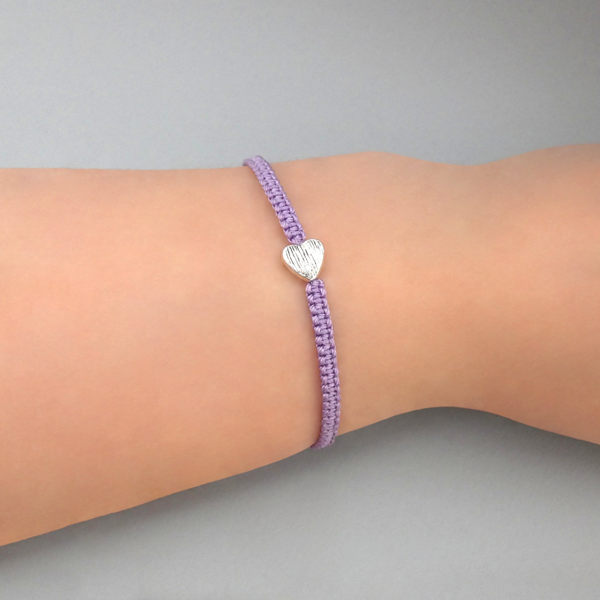 Orchid purple seven inch macramé bracelet with silver plated textured heart charm, lobster clasp and one inch extender chain on a woman's wrist.