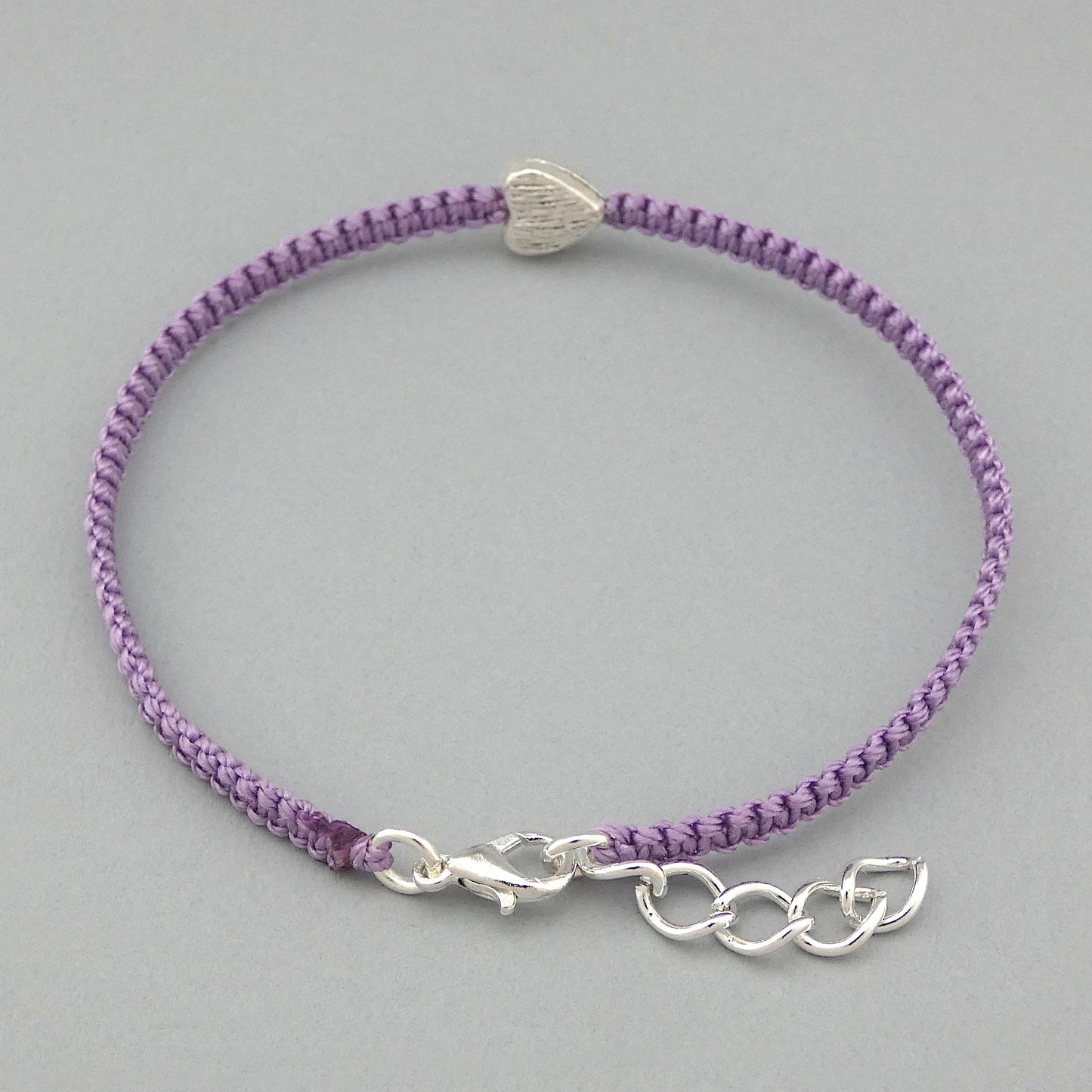 Silver plated lobster claw clasp and one inch extender chain on an orchid purple seven inch macramé bracelet with silver plated textured heart charm.