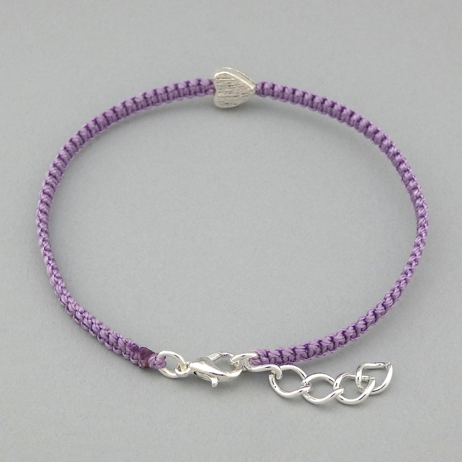 Silver plated lobster claw clasp and one inch extender chain on an orchid purple seven inch macramé bracelet with silver plated textured heart charm.