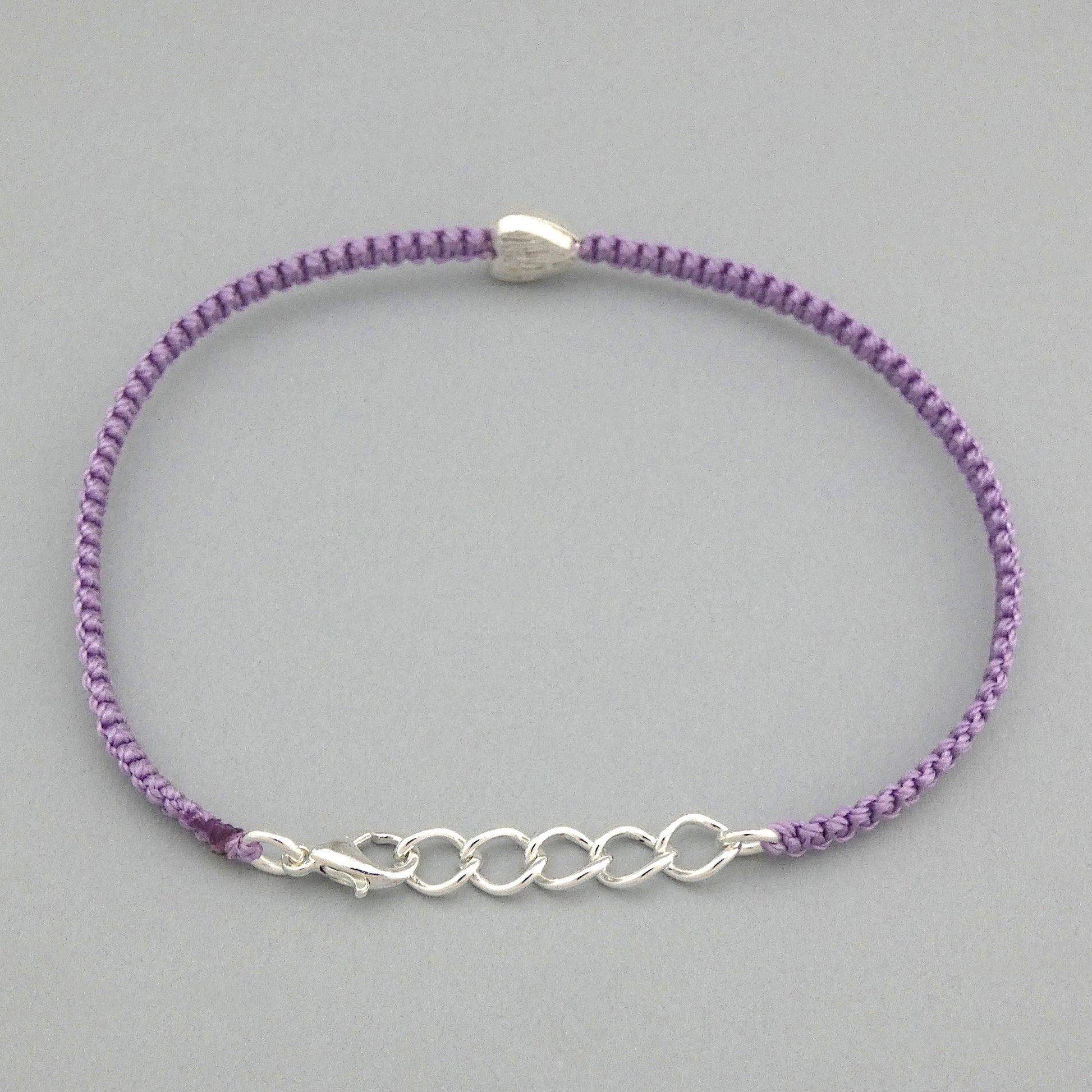 Orchid purple seven inch macramé bracelet with silver plated textured heart charm, lobster clasp and one inch extender chain. The bracelet is fully extending with the extender chain.