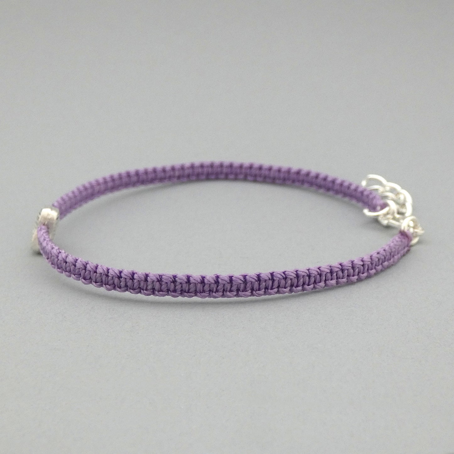 Side view of the knots on an orchid purple seven inch macramé bracelet with silver plated textured heart charm, lobster clasp and one inch extender chain.