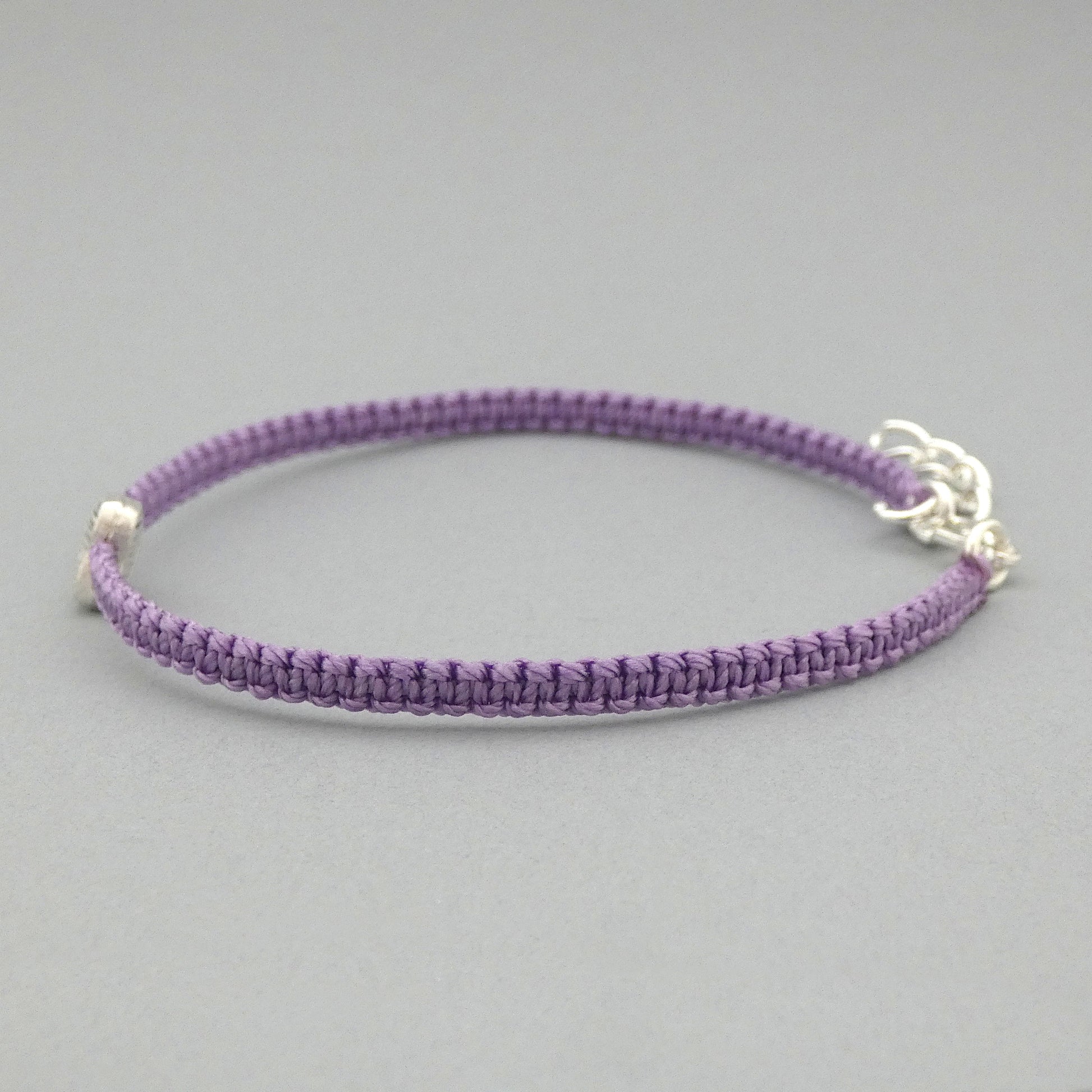 Side view of the knots on an orchid purple seven inch macramé bracelet with silver plated textured heart charm, lobster clasp and one inch extender chain.