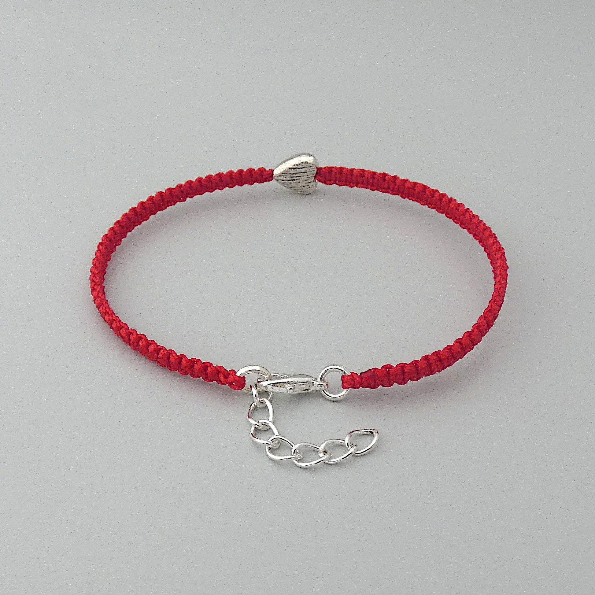 Silver plated lobster claw clasp and one inch extender chain on a red seven inch macramé bracelet with silver plated textured heart charm.