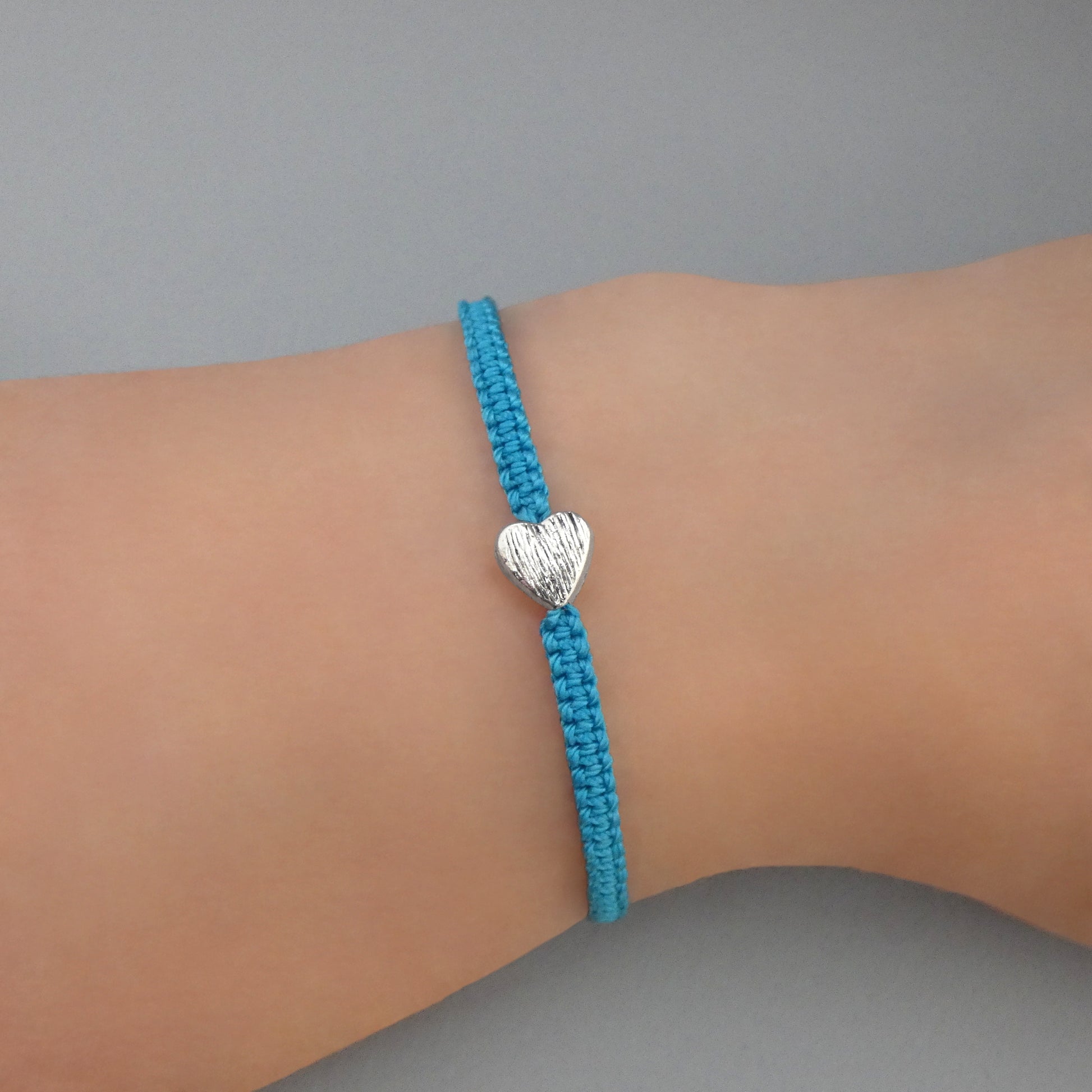 Blue seven inch macramé bracelet with silver plated textured heart charm, lobster clasp and one inch extender chain on a woman's wrist.