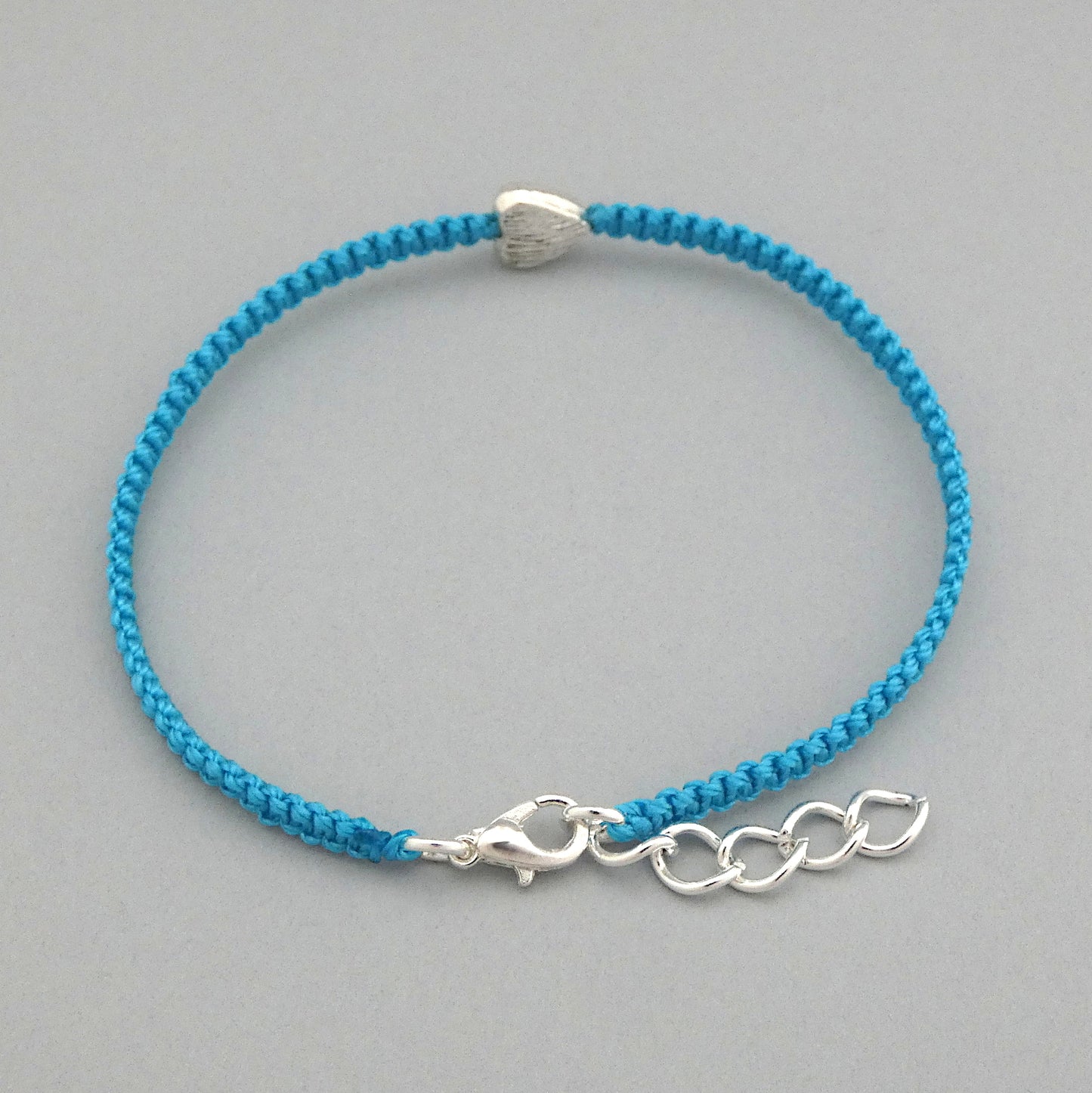 Close up of the lobster claw clasp on a blue seven inch macramé bracelet with silver plated textured heart charm, lobster clasp and one inch extender chain.
