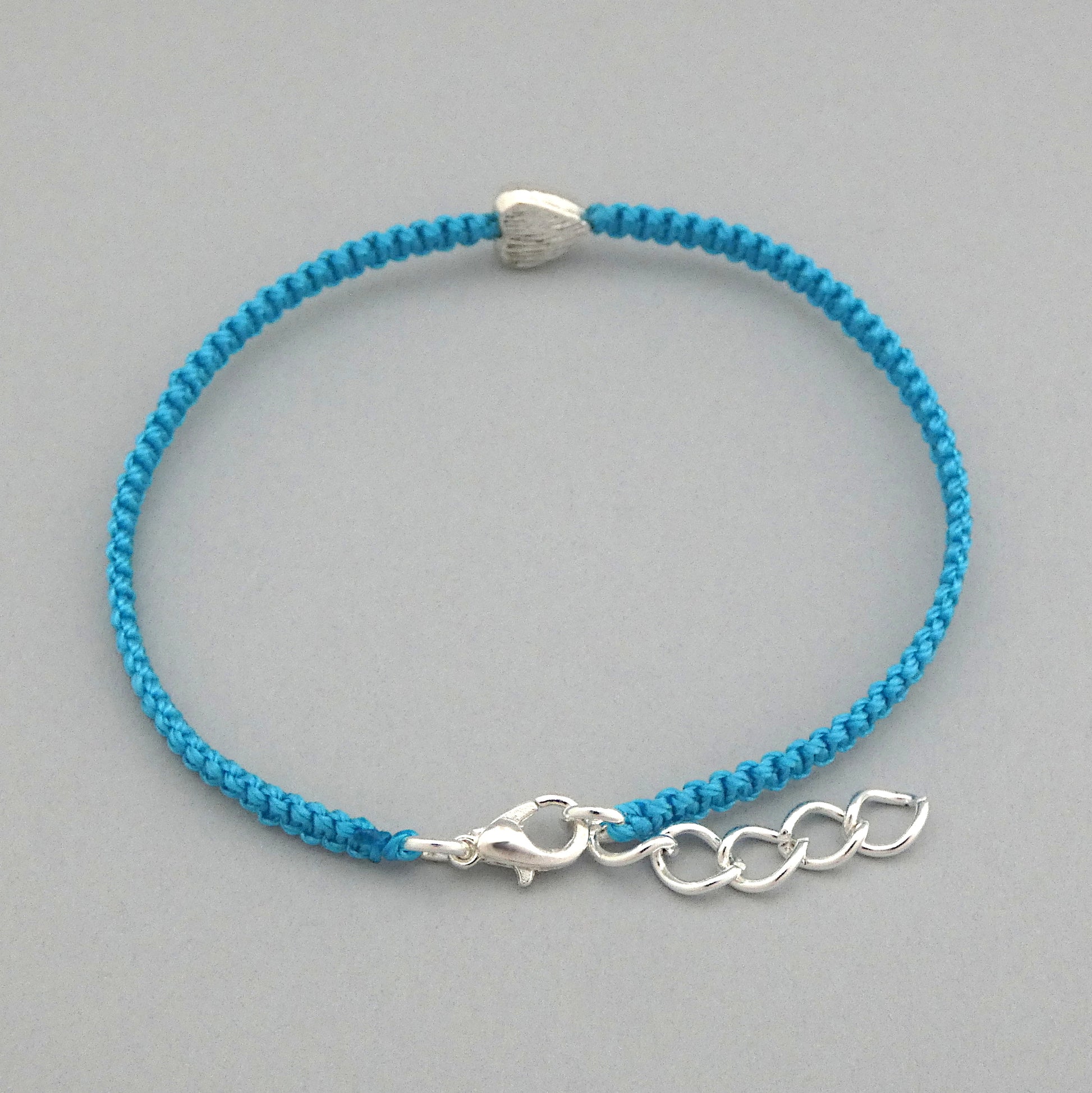 Close up of the lobster claw clasp on a blue seven inch macramé bracelet with silver plated textured heart charm, lobster clasp and one inch extender chain.
