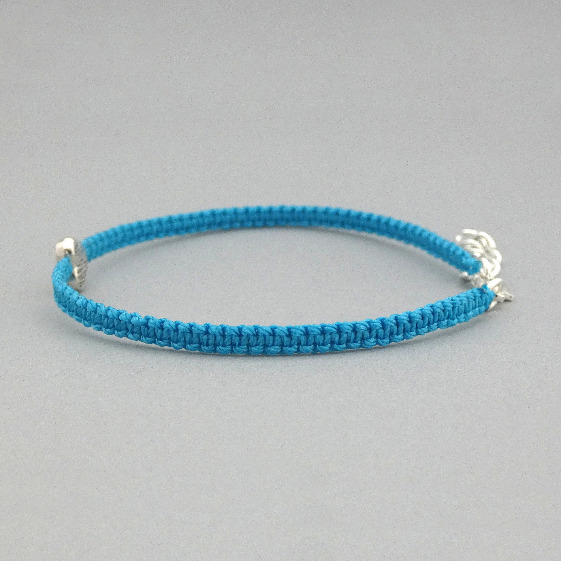 Side view of the knots on a blue seven inch macramé bracelet with silver plated textured heart charm, lobster clasp and one inch extender chain.