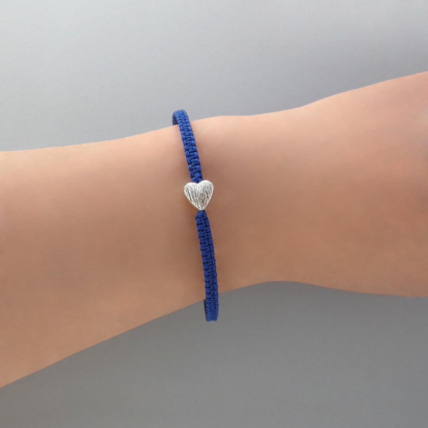 Royal blue seven inch macramé bracelet with silver plated textured heart charm, lobster clasp and one inch extender chain on a woman's wrist.