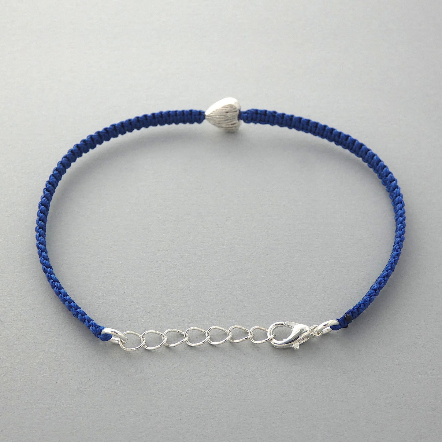 Silver plated lobster claw clasp attached to the end on a one inch extender chain on a Royal blue seven inch macramé bracelet with silver plated textured heart charm.