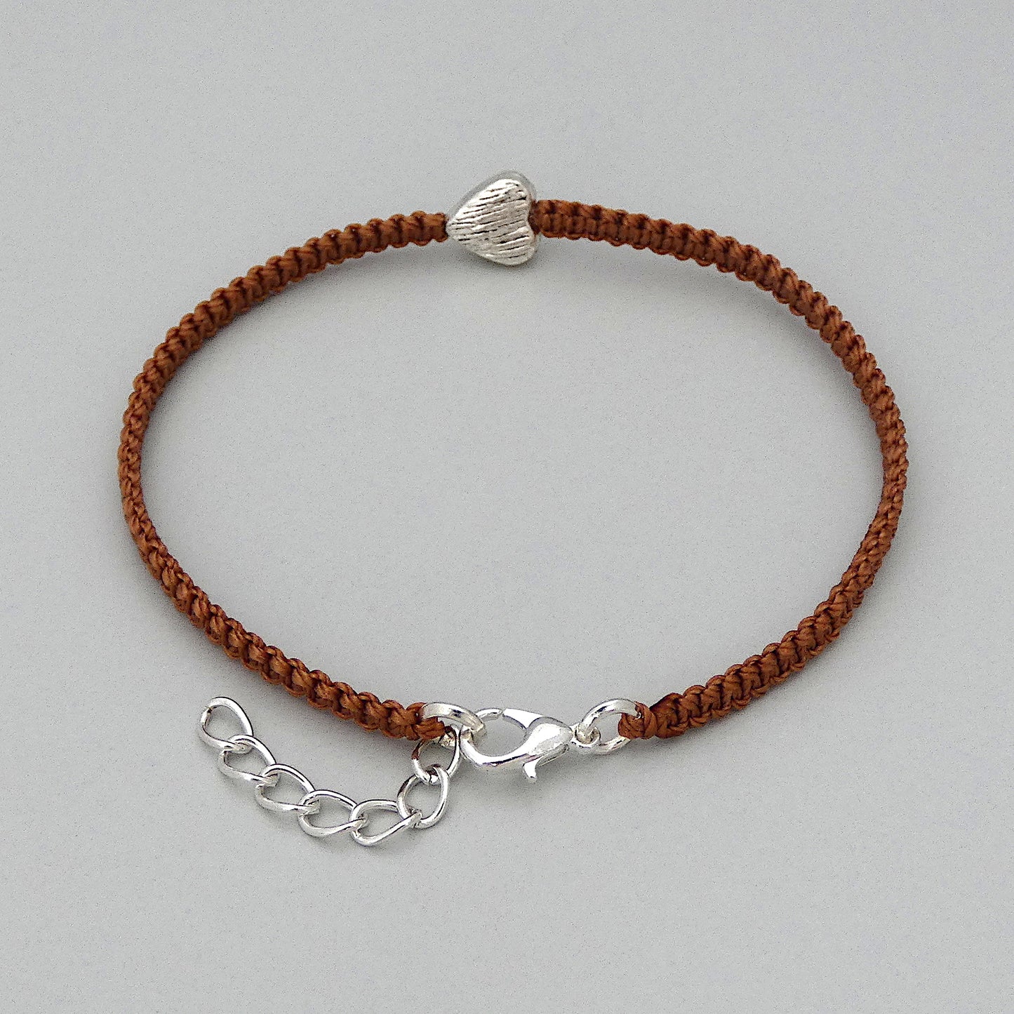 Silver plated lobster claw clasp and one inch extender chain on a copper coloured seven inch macramé bracelet with silver plated textured heart charm.