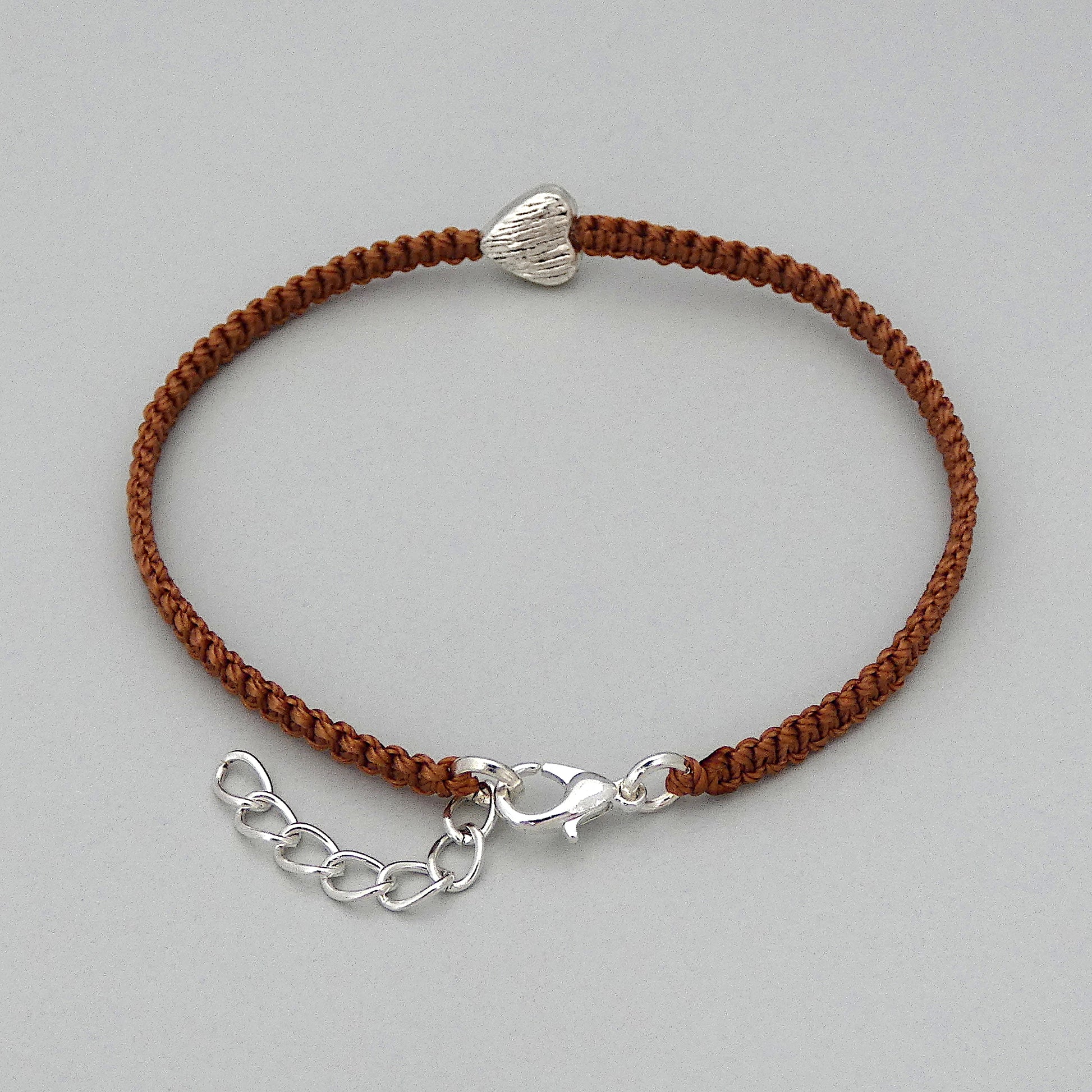 Silver plated lobster claw clasp and one inch extender chain on a copper coloured seven inch macramé bracelet with silver plated textured heart charm.
