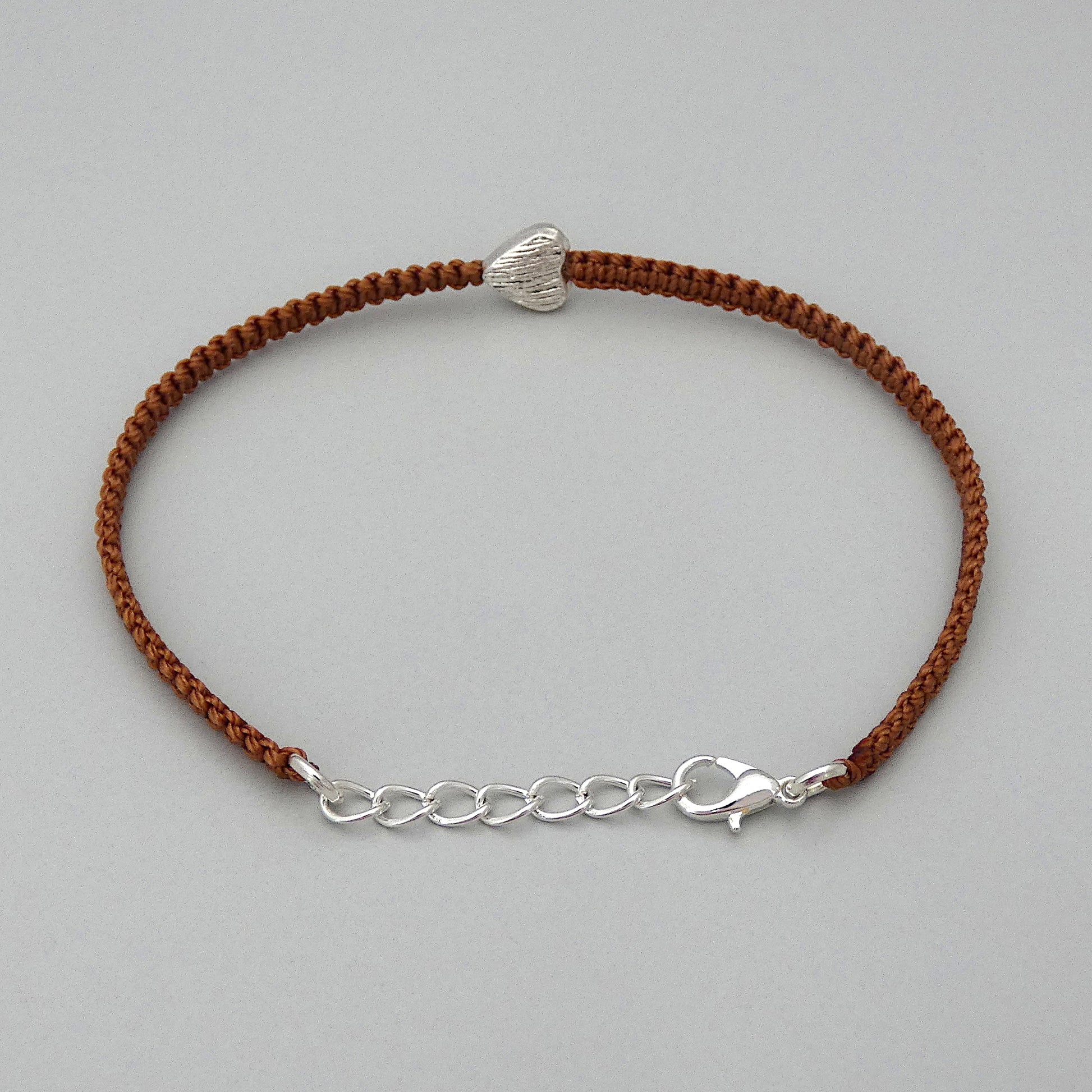 Silver plated lobster claw clasp attached to the end of a one inch extender chain on a copper coloured seven inch macramé bracelet with silver plated textured heart charm.