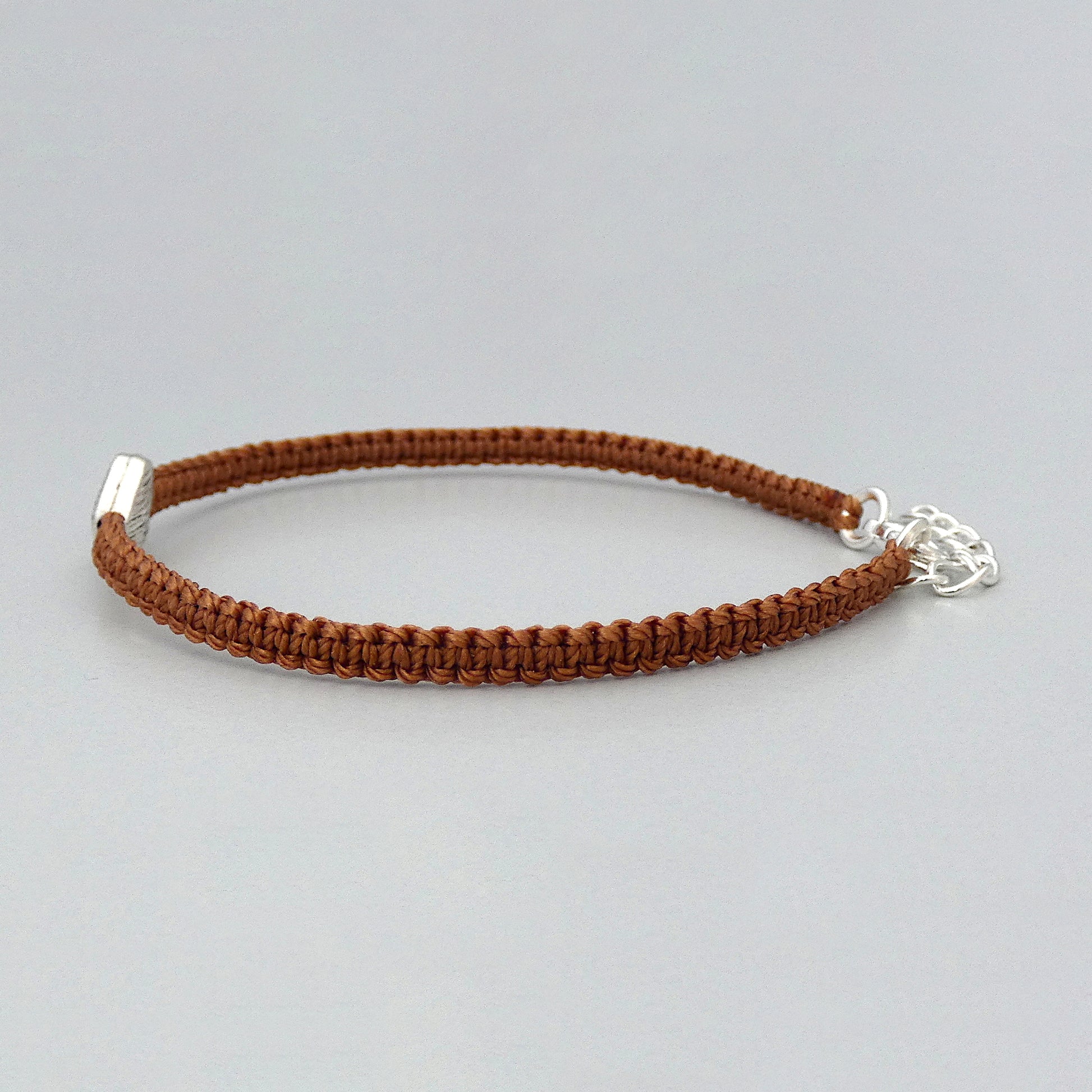 Side view of the knots on a copper coloured seven inch macramé bracelet with silver plated textured heart charm.