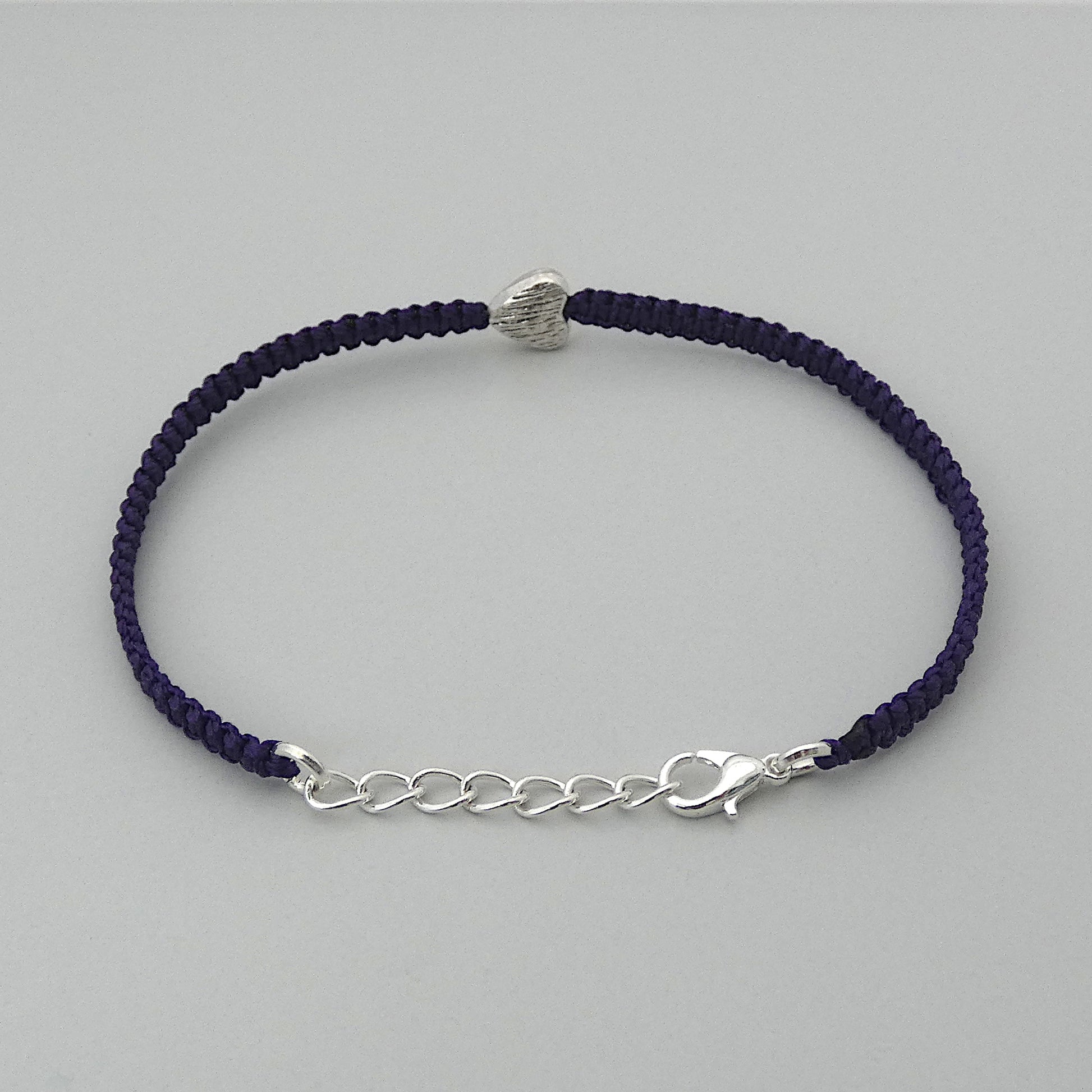 Dark purple seven inch macramé bracelet with silver plated textured heart charm, lobster clasp and one inch extender chain. The bracelet is fully extended on the extender chain.