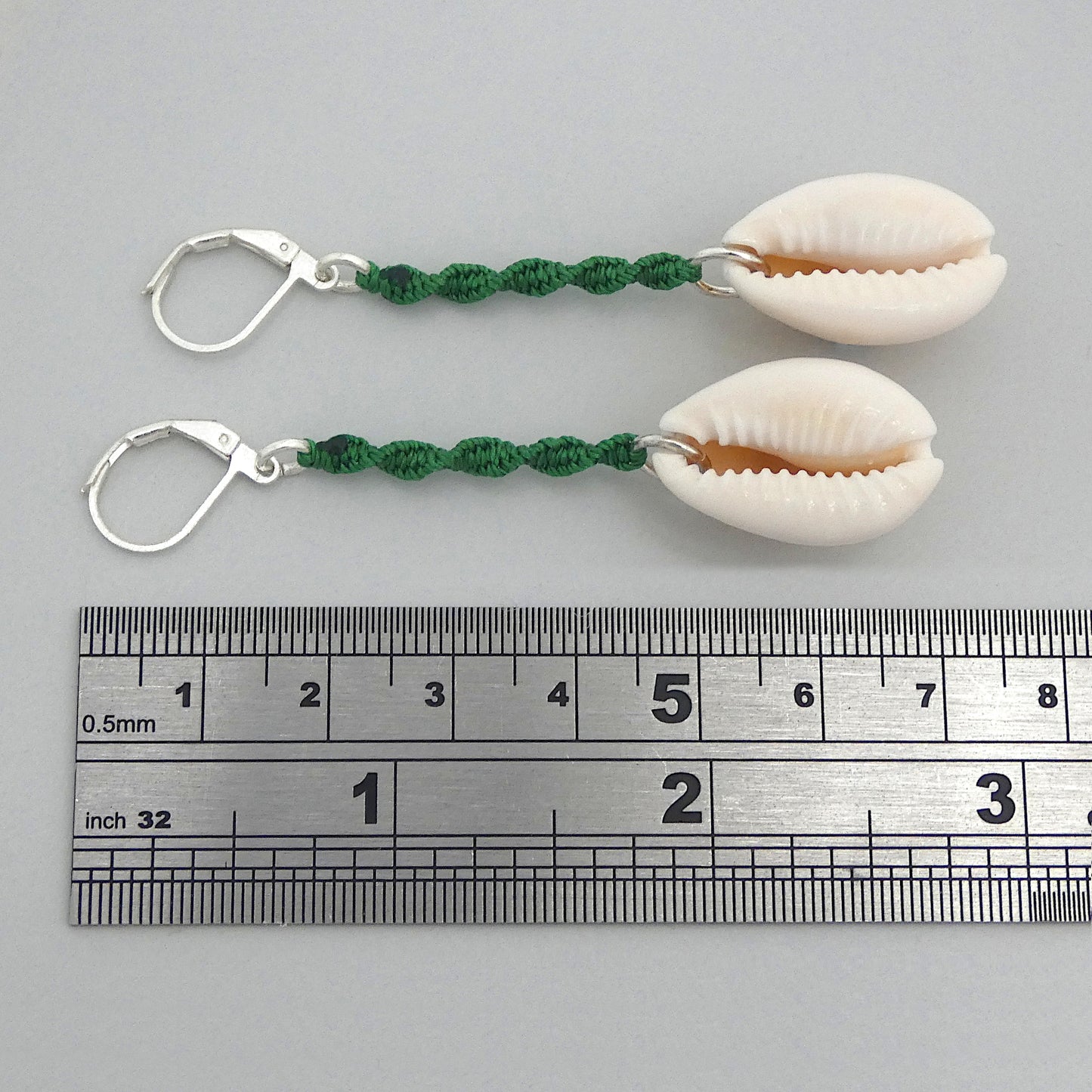 Silver plated leverback earrings with cowrie shells and green macramé twist detail.