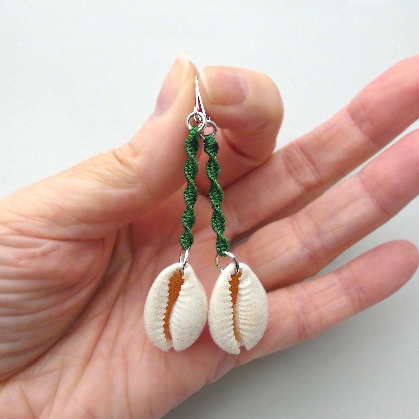 Silver plated leverback earrings with cowrie shells and green macramé twist detail.