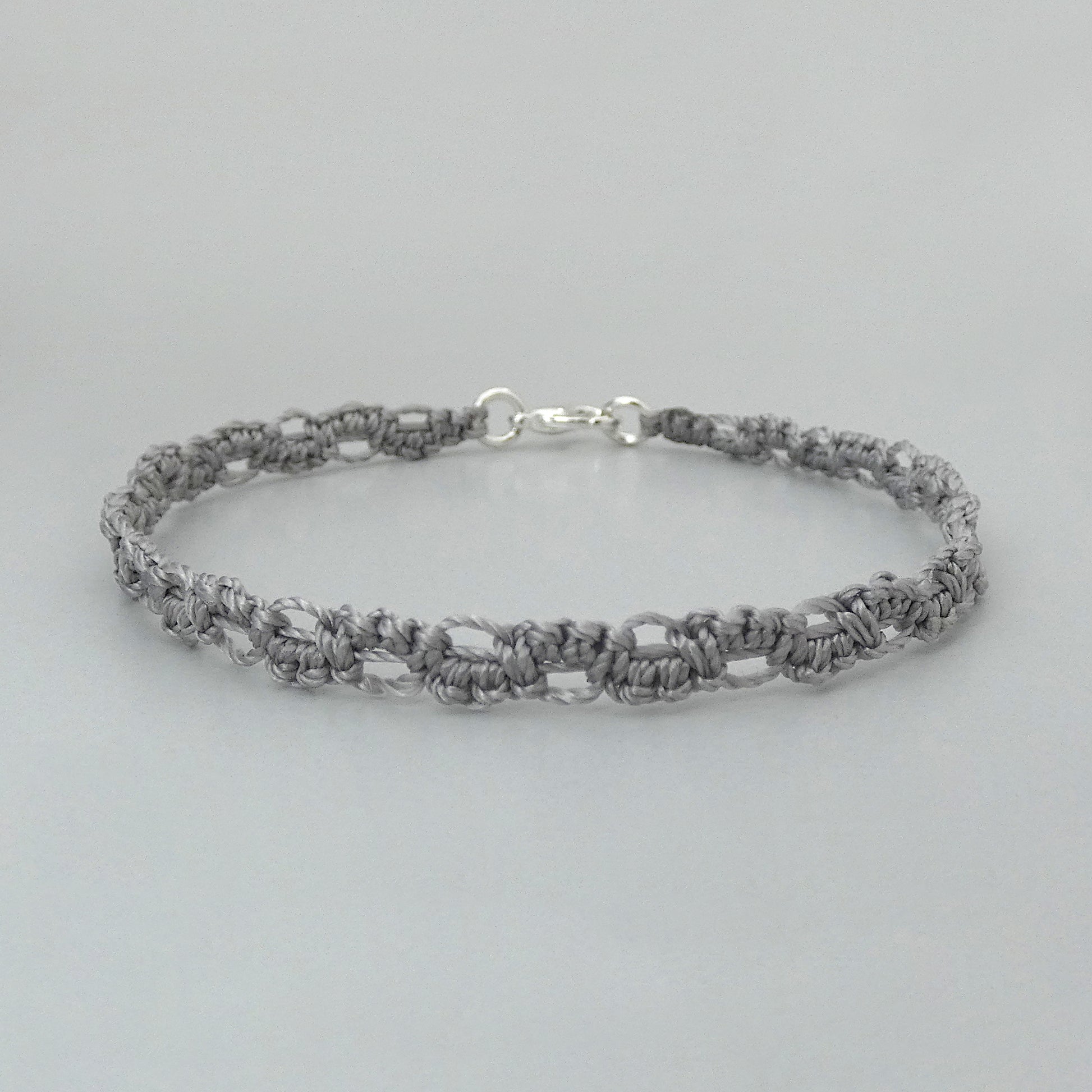 A silver grey macramé bracelet with a shiny silver plated clasp, displayed against a neutral background.