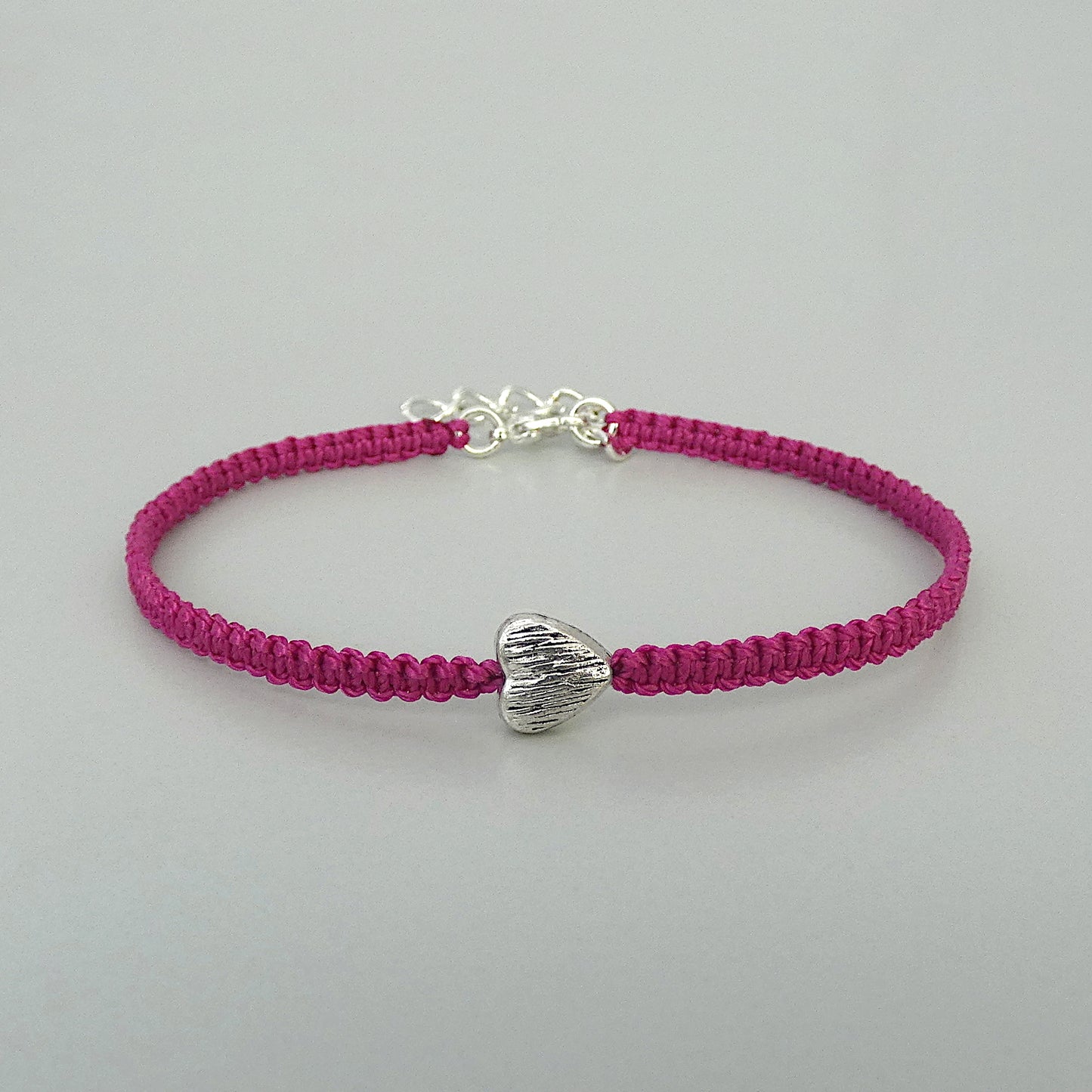 Magenta seven inch macramé bracelet with silver plated textured heart charm, lobster clasp and one inch extender chain.
