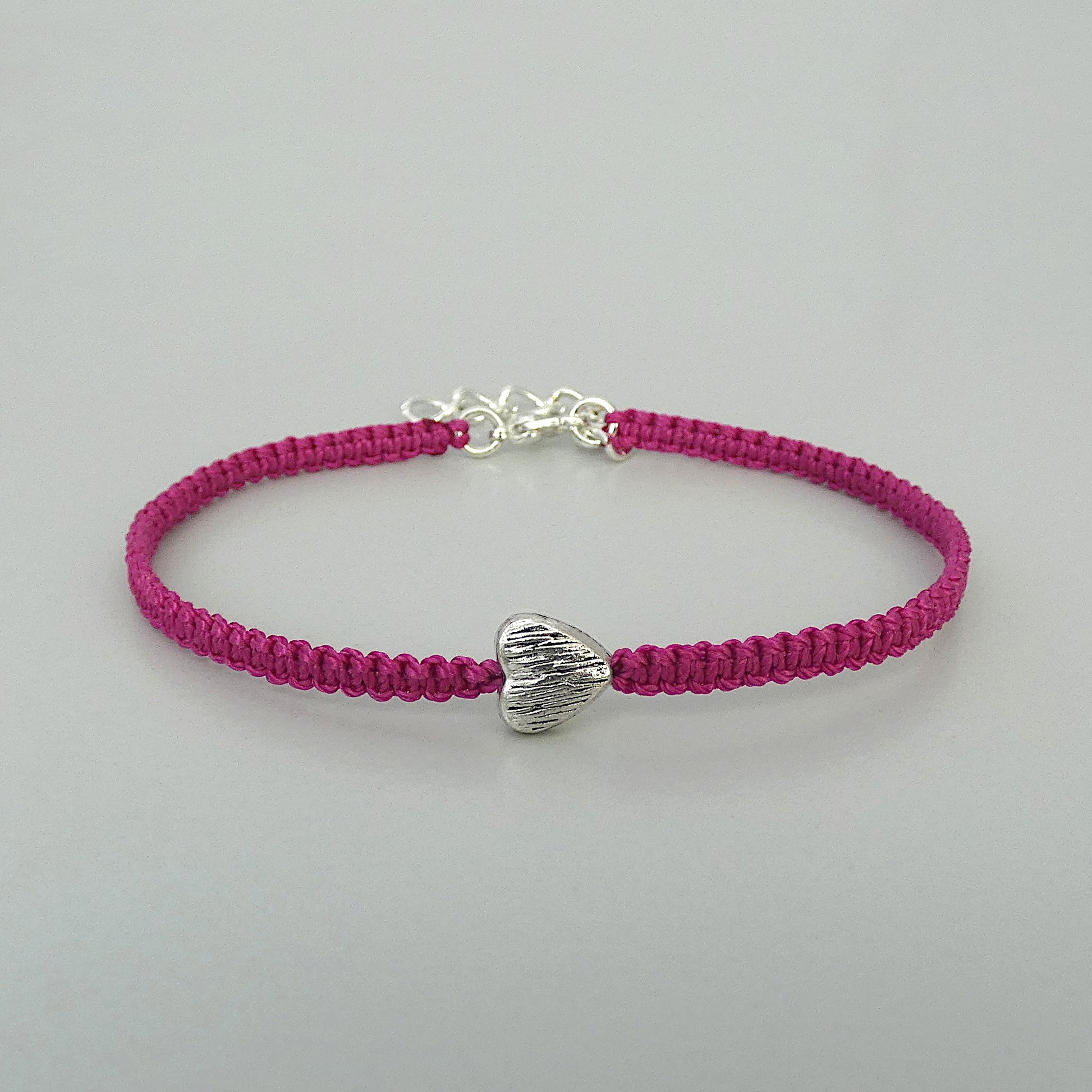 Magenta seven inch macramé bracelet with silver plated textured heart charm, lobster clasp and one inch extender chain.
