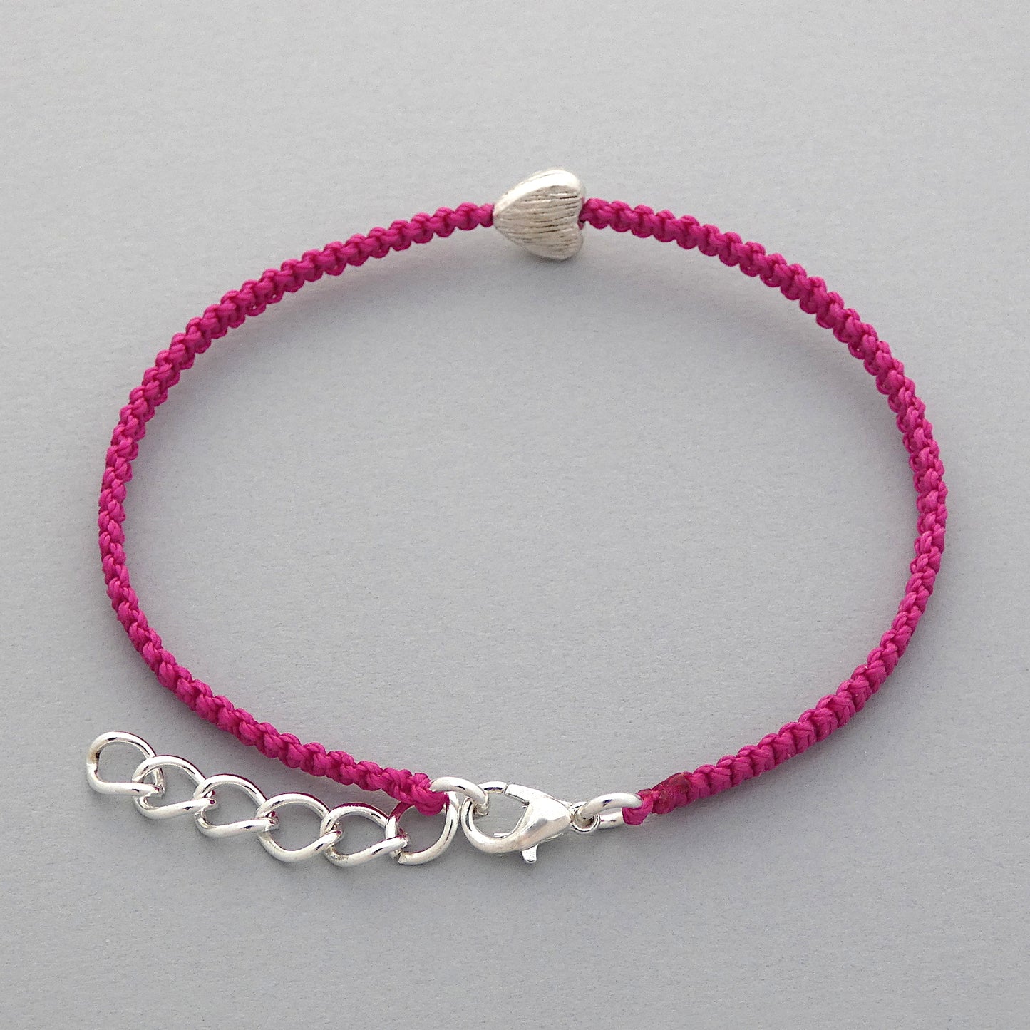 Silver plated lobster claw clasp and one inch extender chain on a magenta seven inch macramé bracelet with silver plated textured heart charm.
