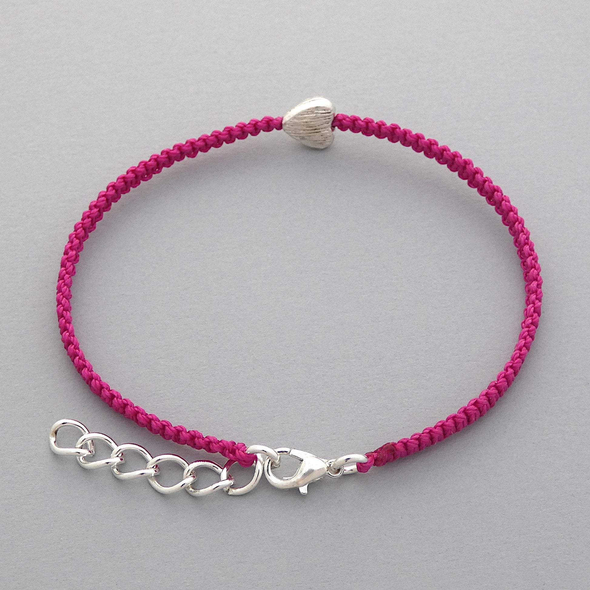 Silver plated lobster claw clasp and one inch extender chain on a magenta seven inch macramé bracelet with silver plated textured heart charm.
