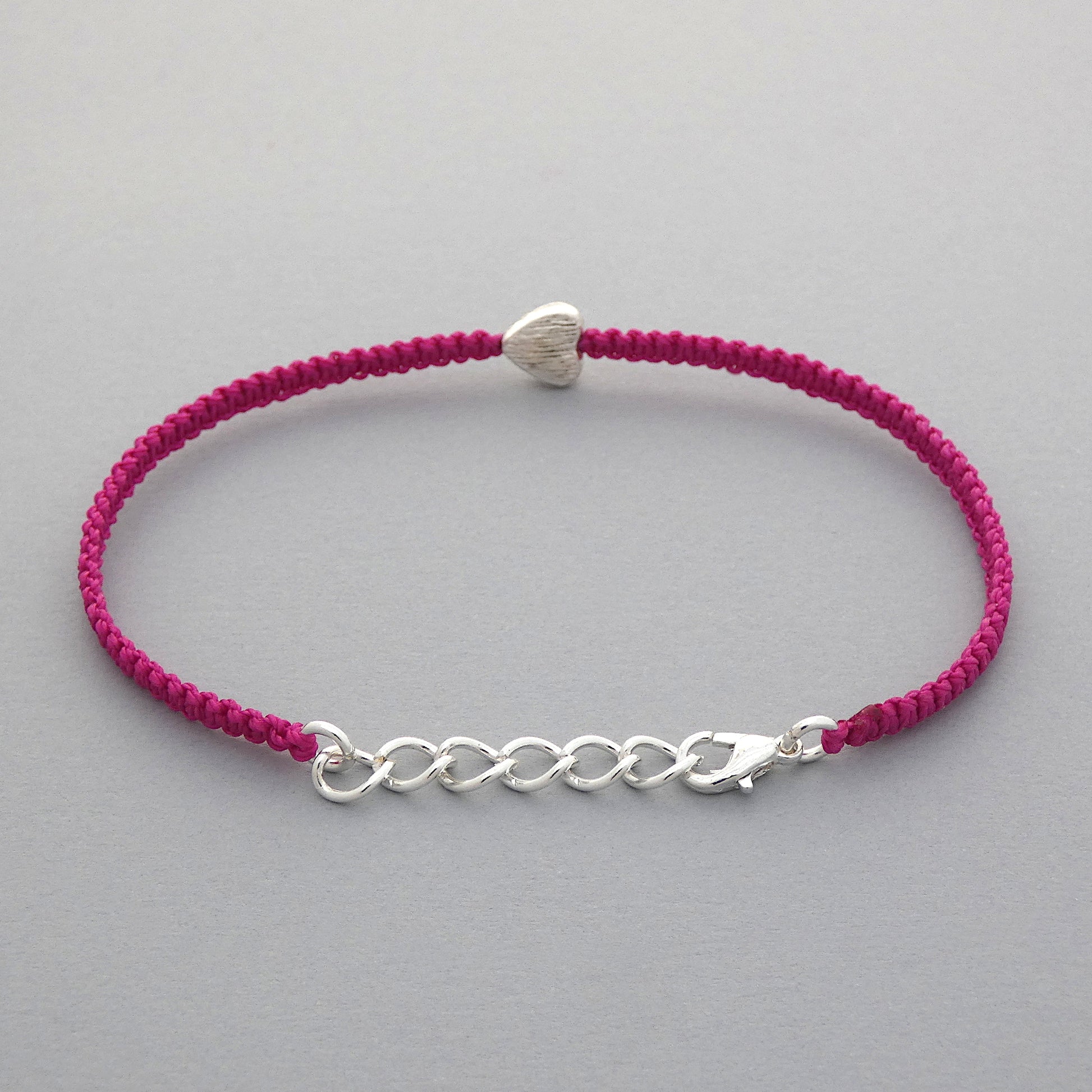 Silver plated lobster claw clasp attached to a one inch extender chain on  a magenta seven inch macramé bracelet with silver plated textured heart charm.