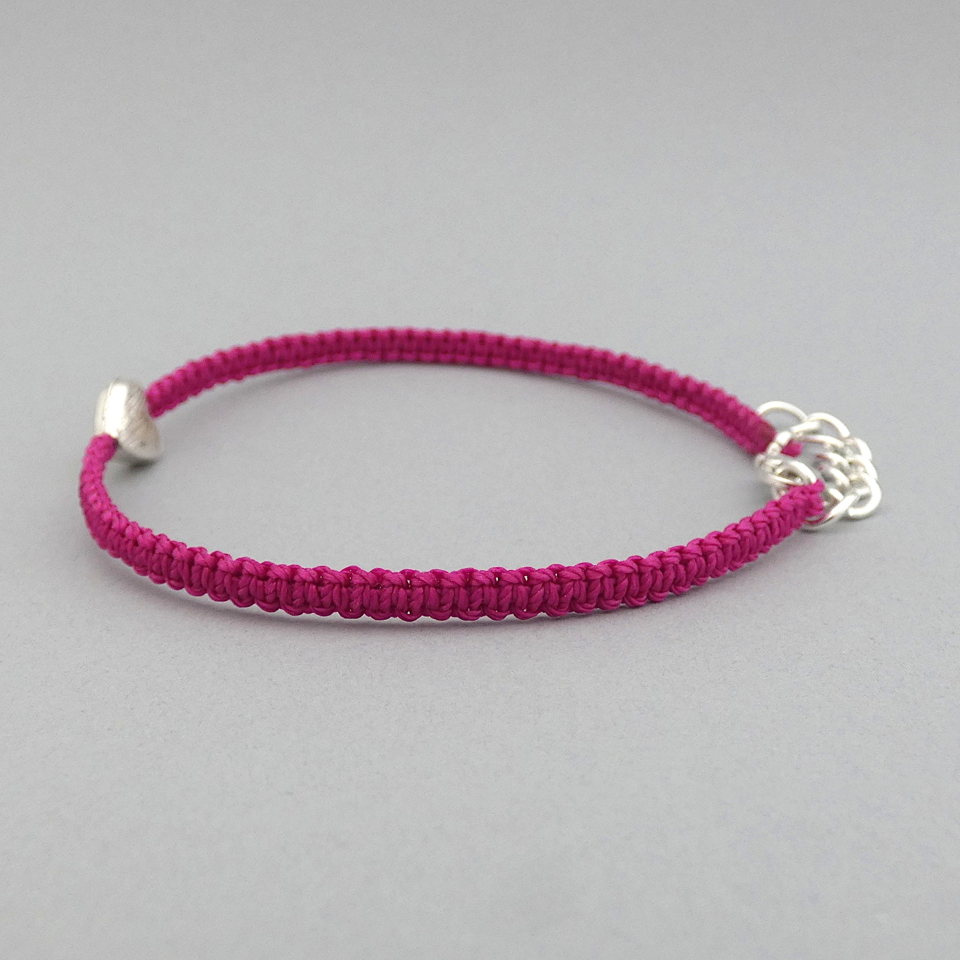 Side view of knots on a magenta seven inch macramé bracelet with silver plated textured heart charm.
