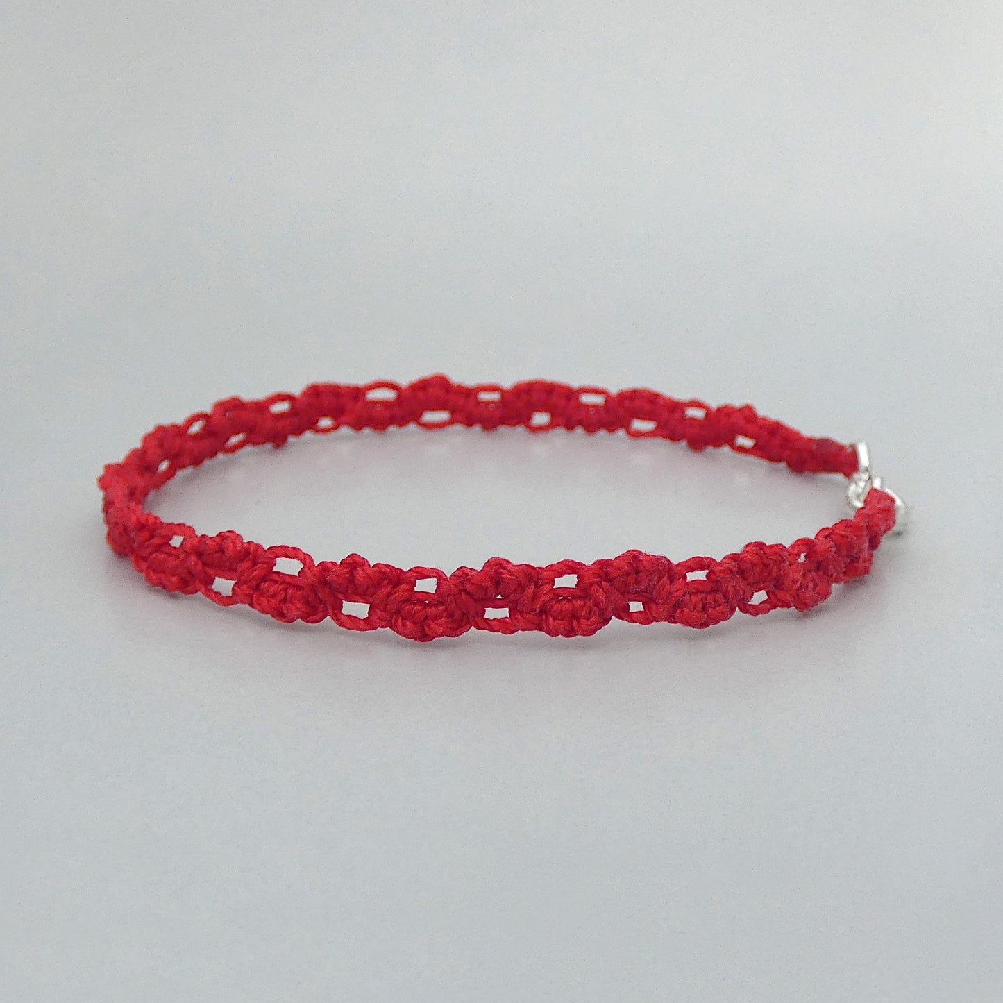 Red macramé bracelet tied with an intricate lace effect with silver plated clasp and optional 1” extender chain.