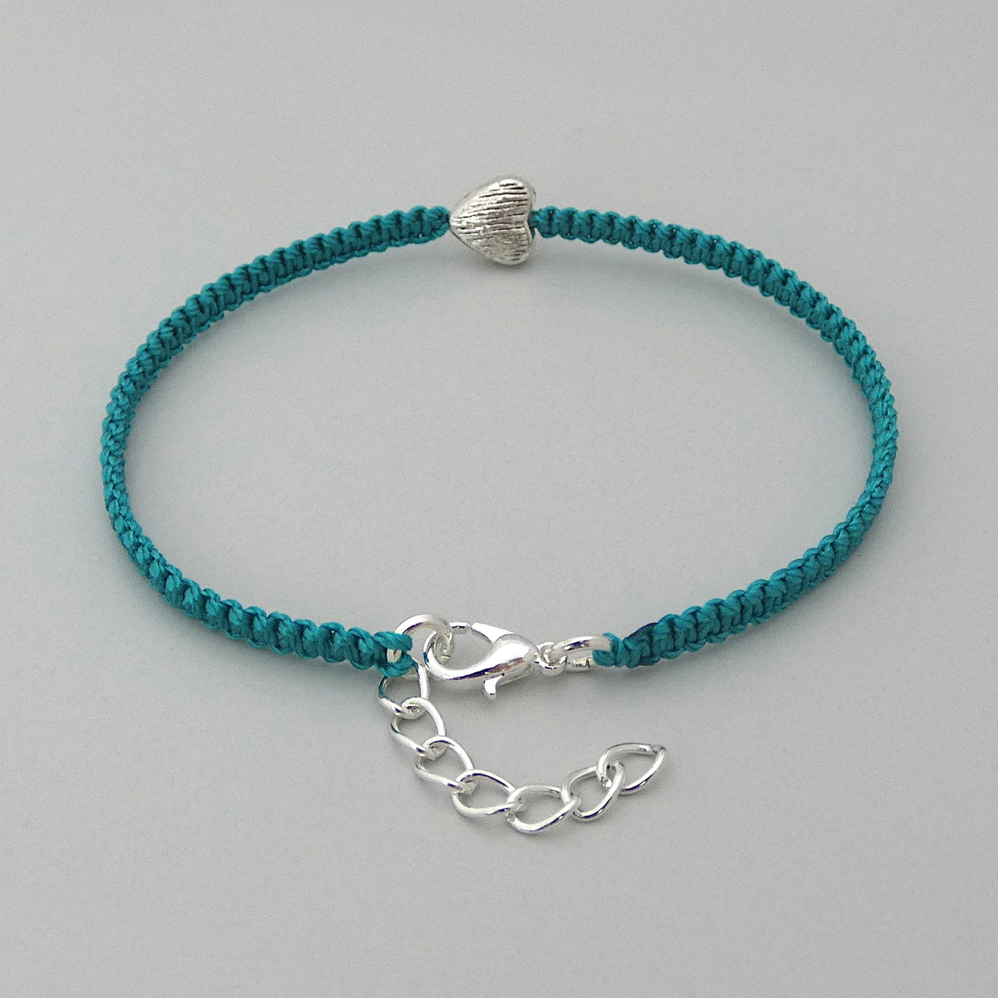 Teal green seven inch macramé bracelet with silver plated textured heart charm, lobster clasp and one inch extender chain with a close up of the clasp.