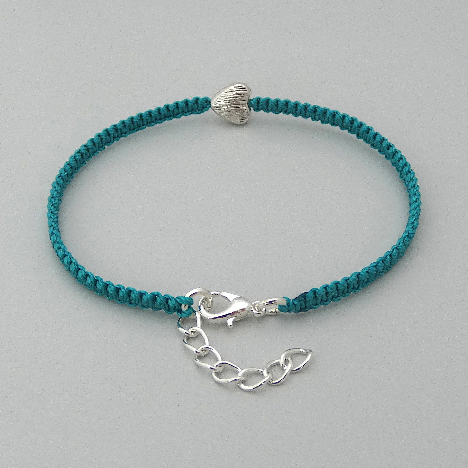Teal green seven inch macramé bracelet with silver plated textured heart charm, lobster clasp and one inch extender chain with a close up of the clasp.