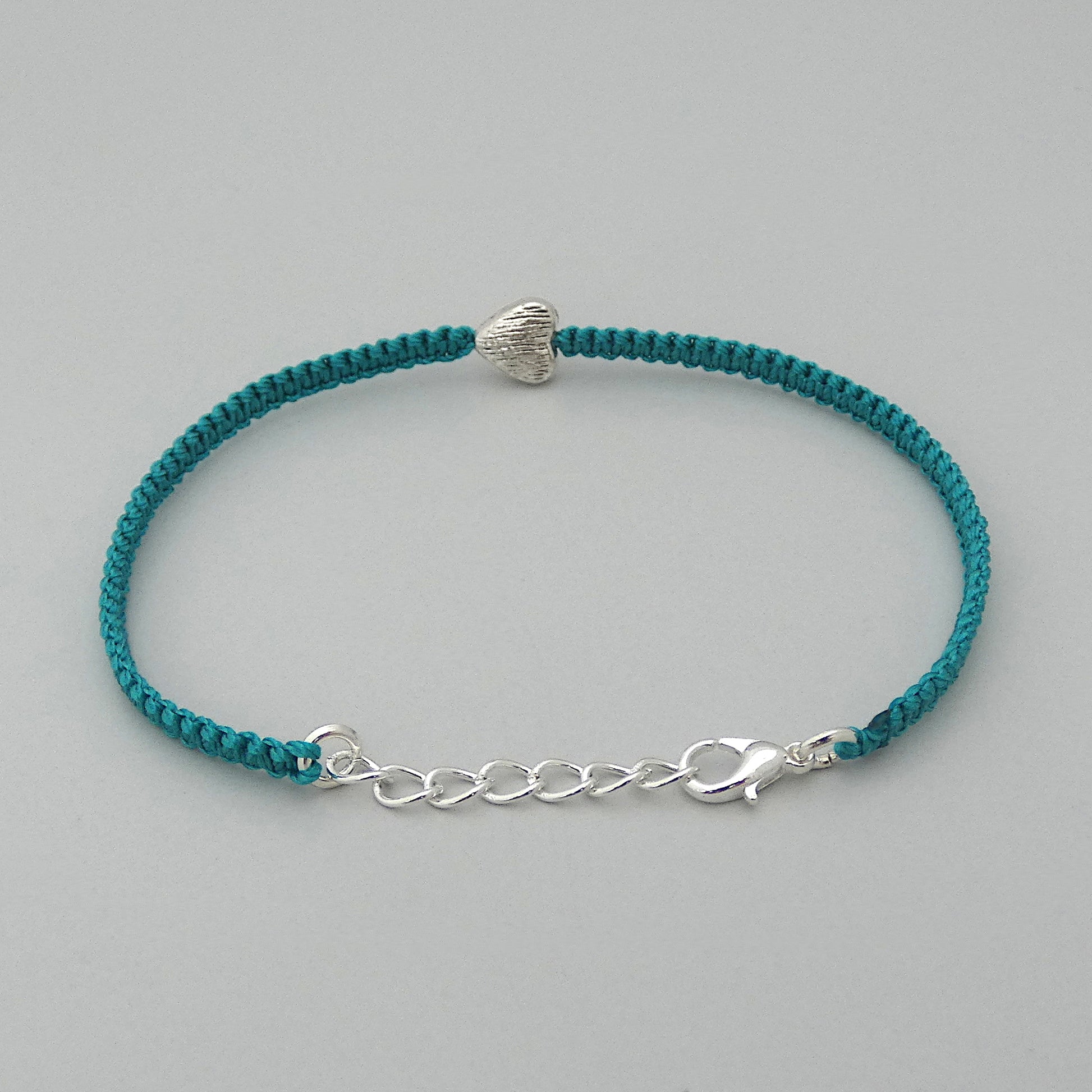 Teal green seven inch macramé bracelet with silver plated textured heart charm, lobster clasp and one inch extender chain with the bracelet fully extended.