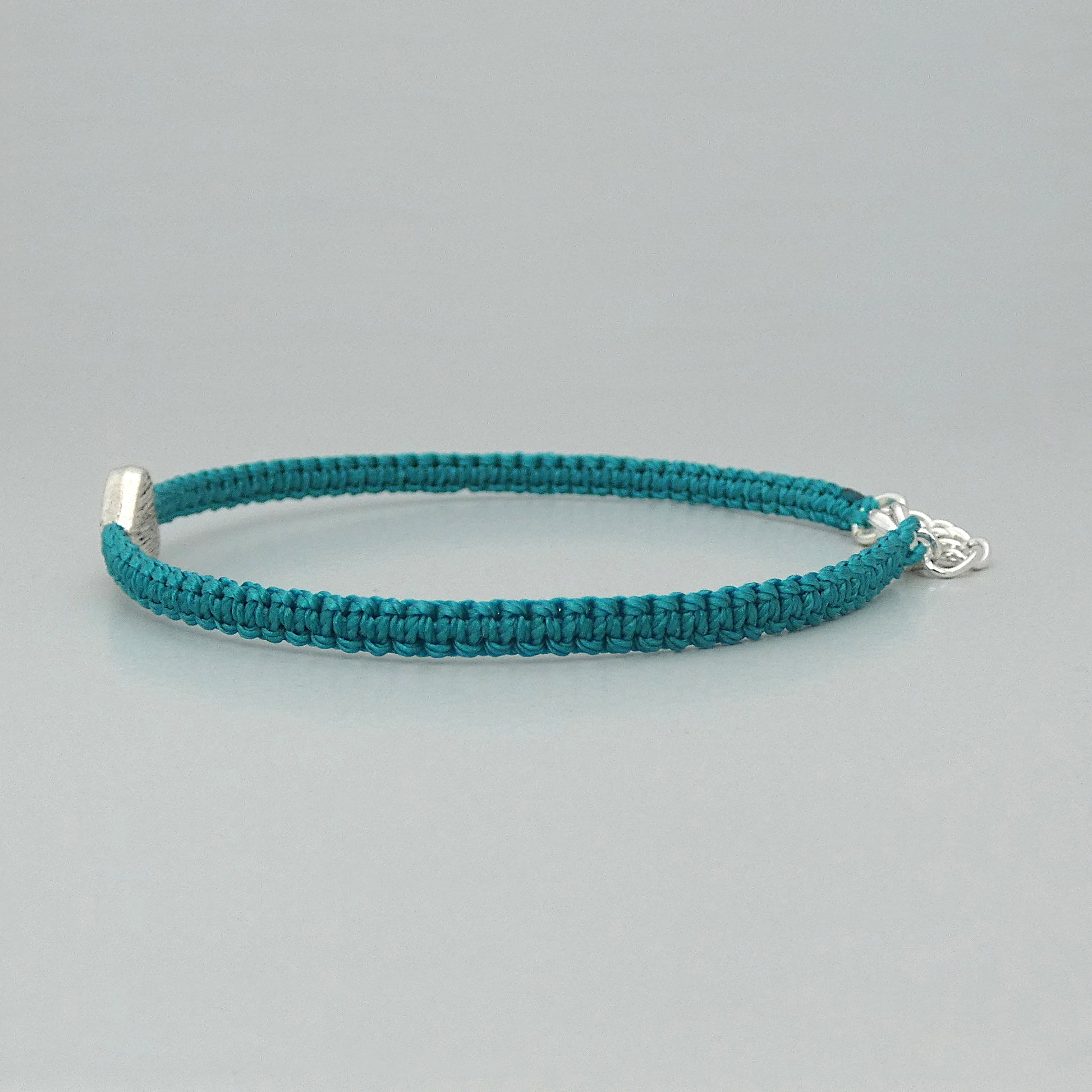 Side view of the knots on a teal green seven inch macramé bracelet with silver plated textured heart charm, lobster clasp and one inch extender chain.