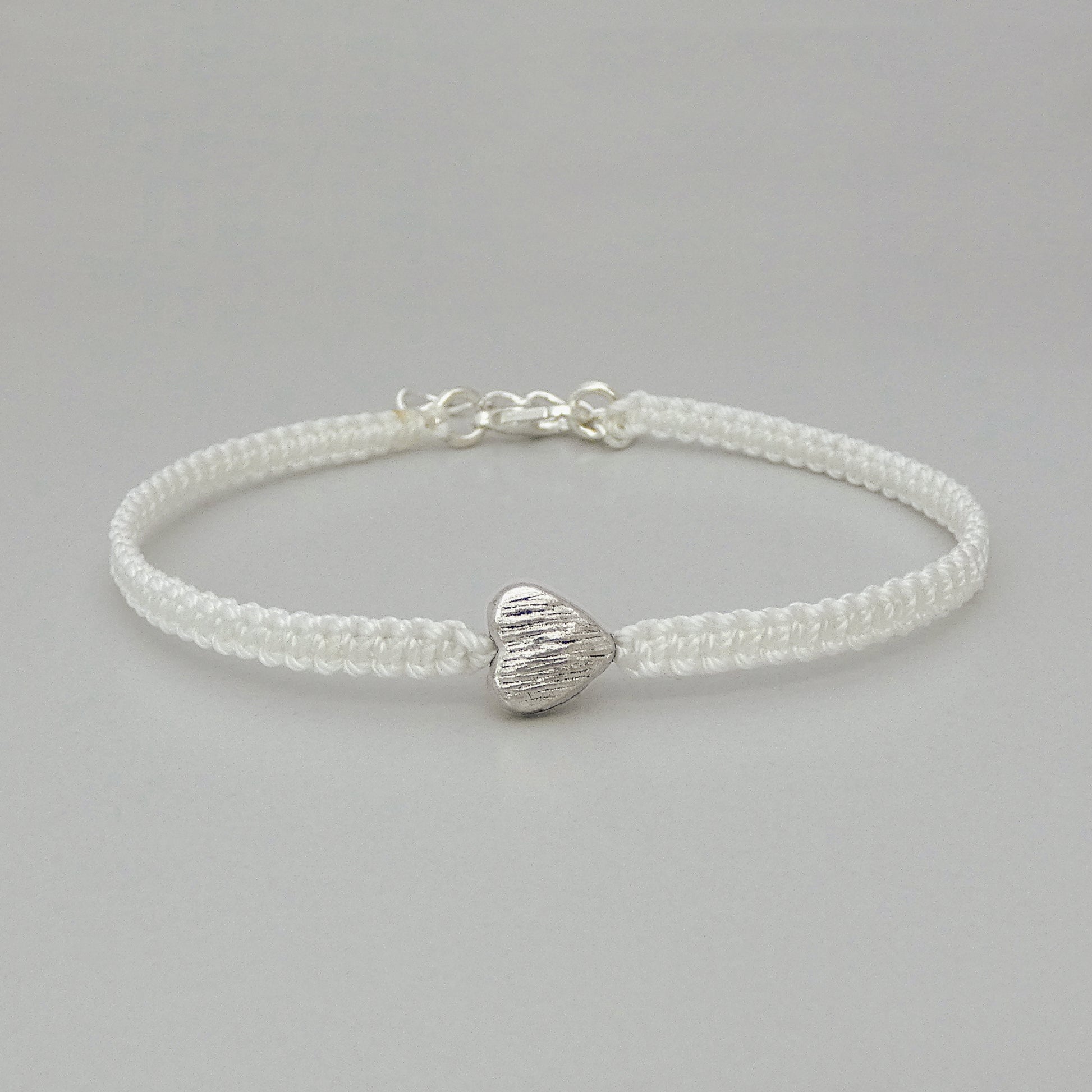 White seven inch macramé bracelet with silver plated textured heart charm, lobster clasp and one inch extender chain.