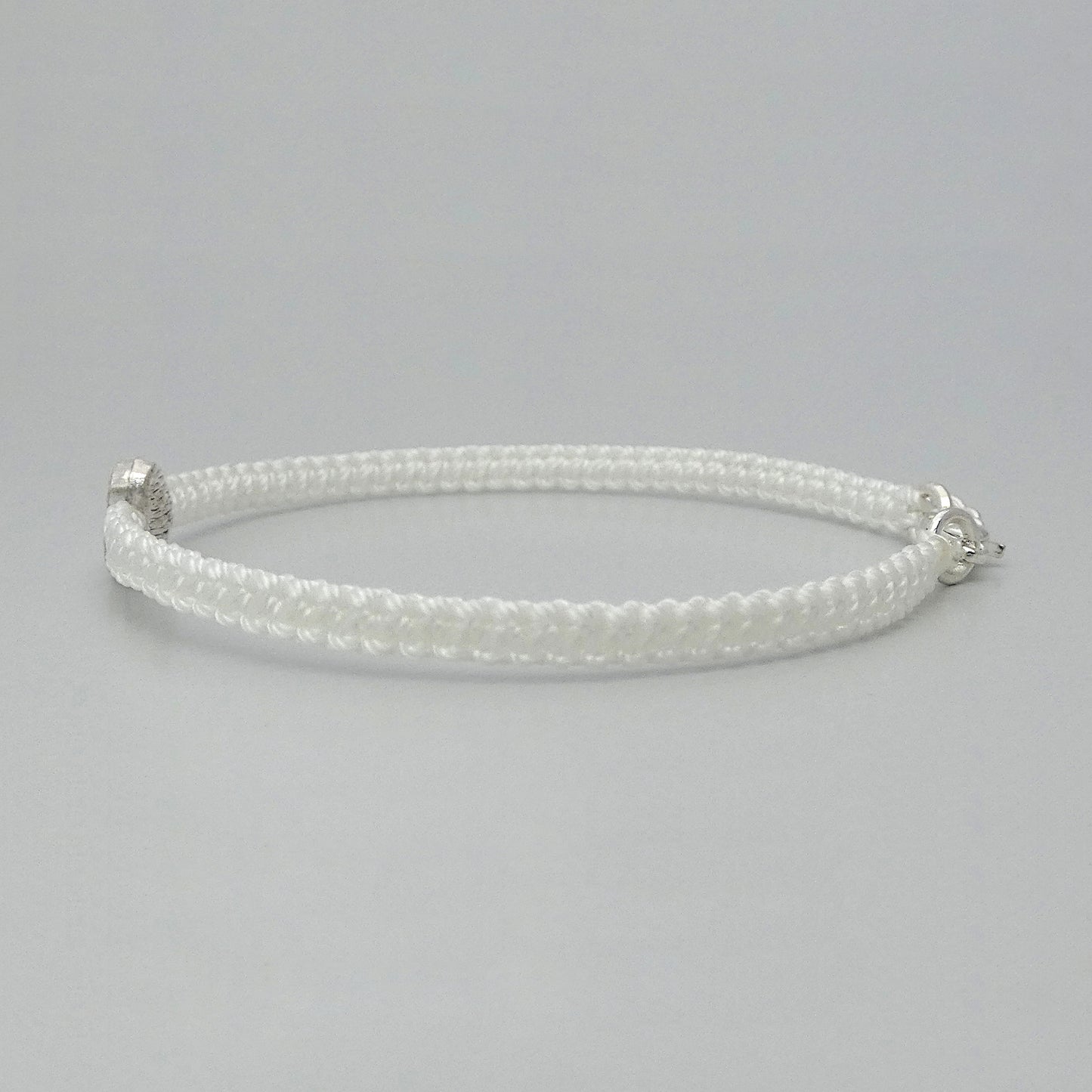 Side view of the knots on a white seven inch macramé bracelet with silver plated textured heart charm.
