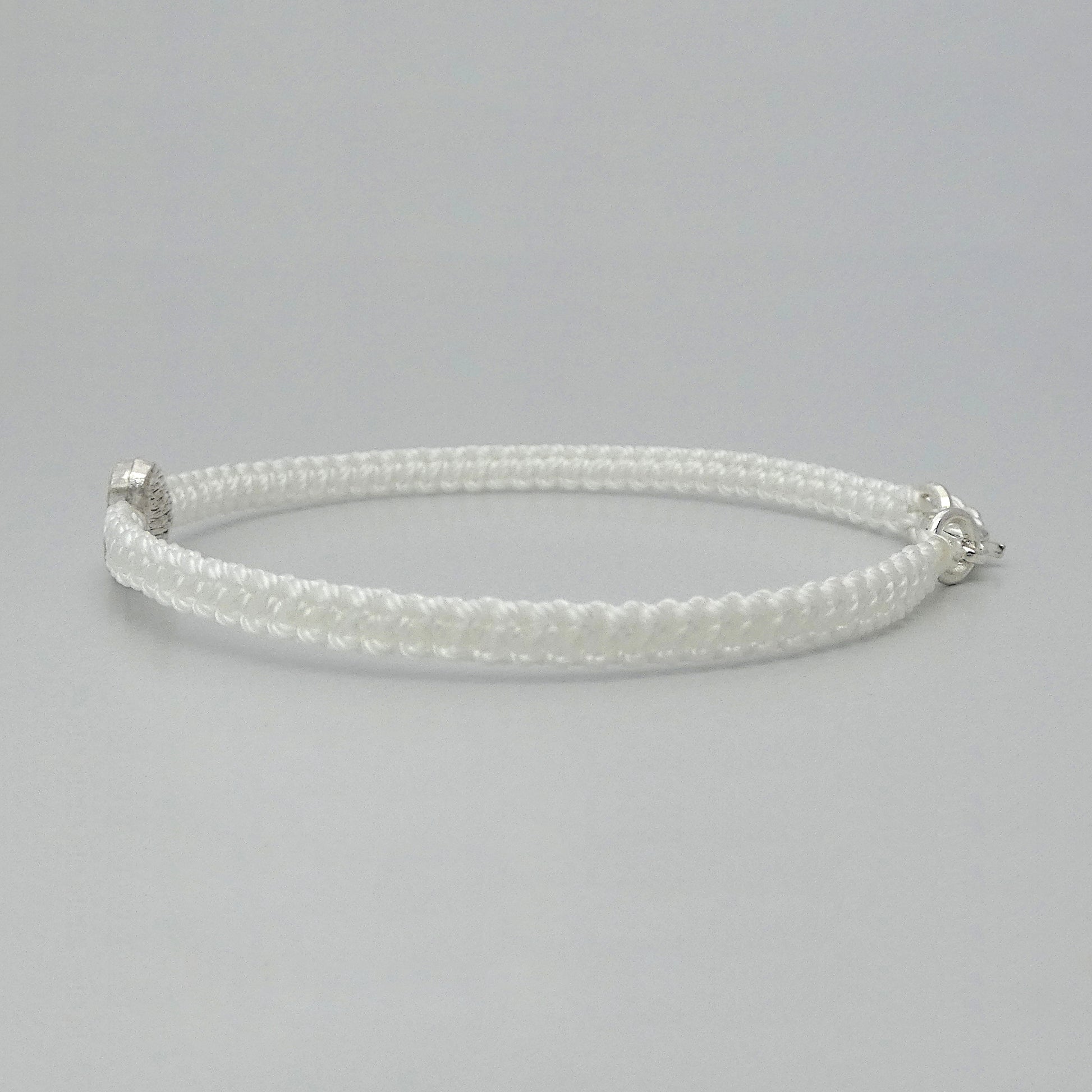 Side view of the knots on a white seven inch macramé bracelet with silver plated textured heart charm.